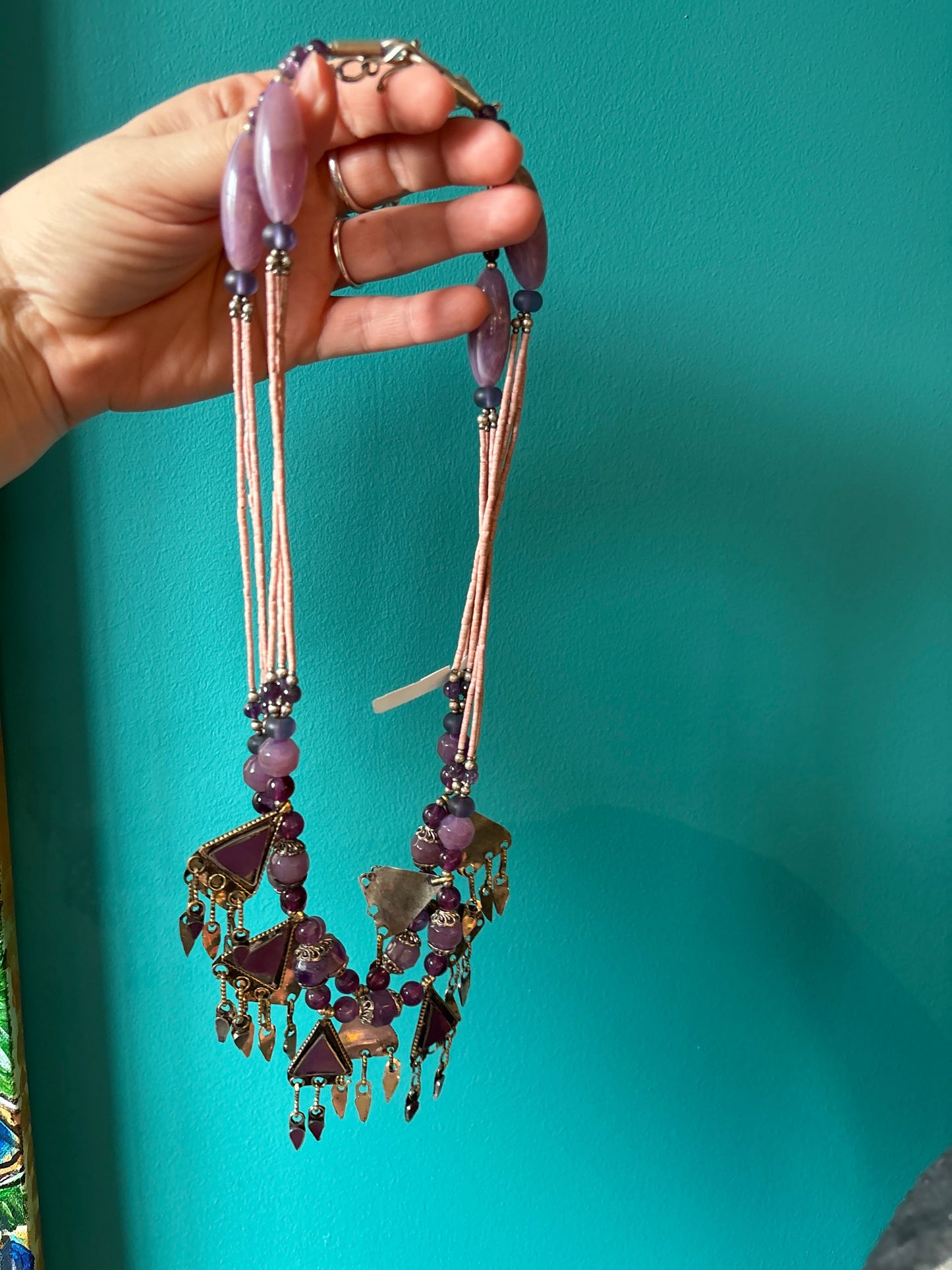 Vintage Afghanistan necklace with purple beads and intricate metal charms held against a teal background