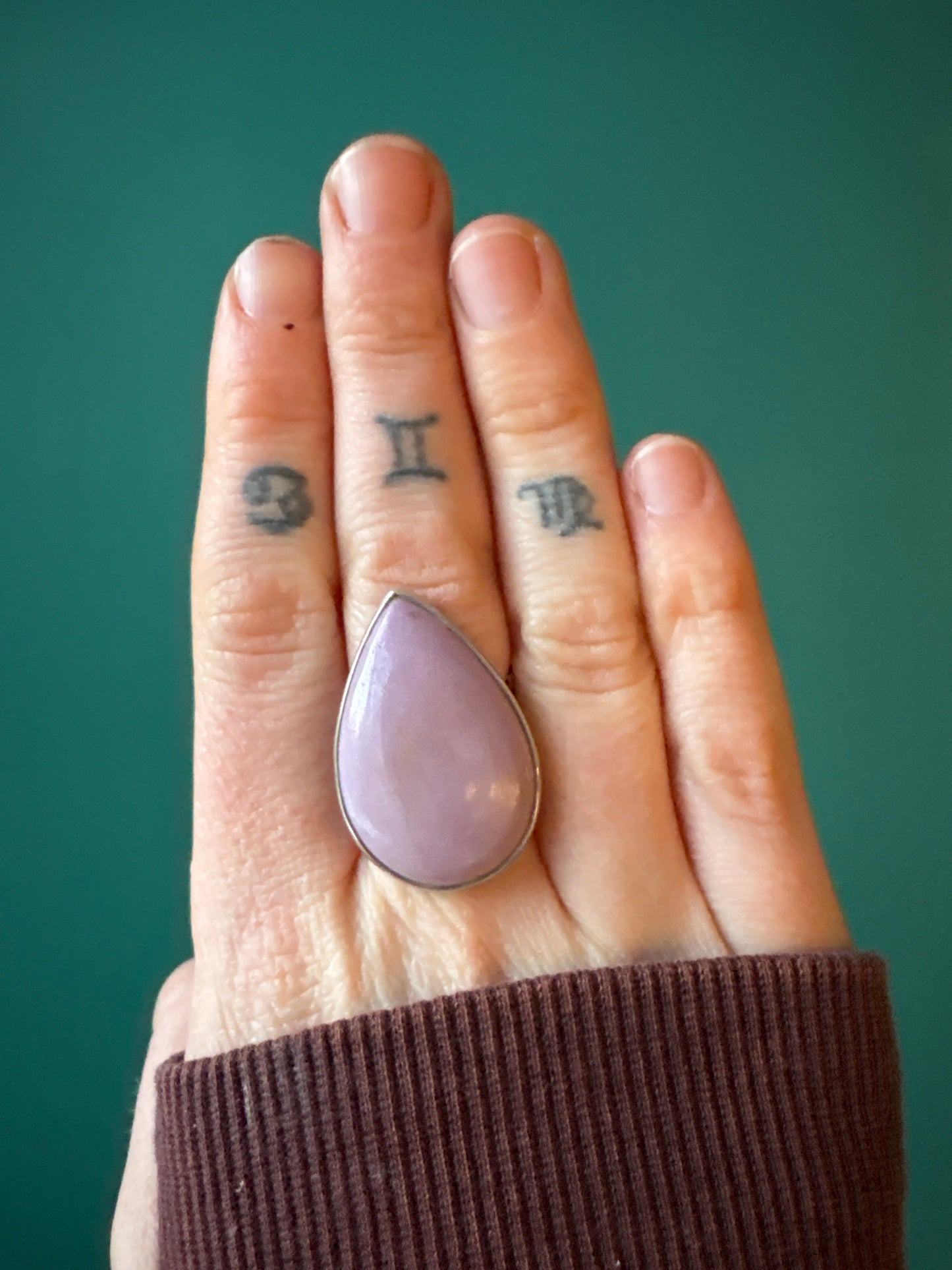 Adjustable Ring Phosphosiderite with teardrop-shaped calming stone on hand with tattoos against teal background