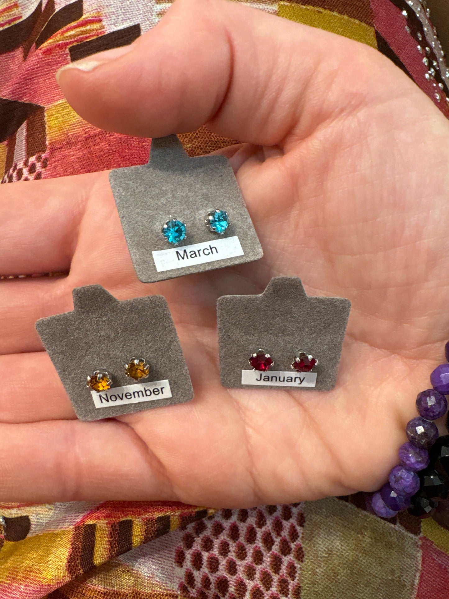 Sterling dipped earrings with birthstone studs for March, November, and January on gray display cards in hand