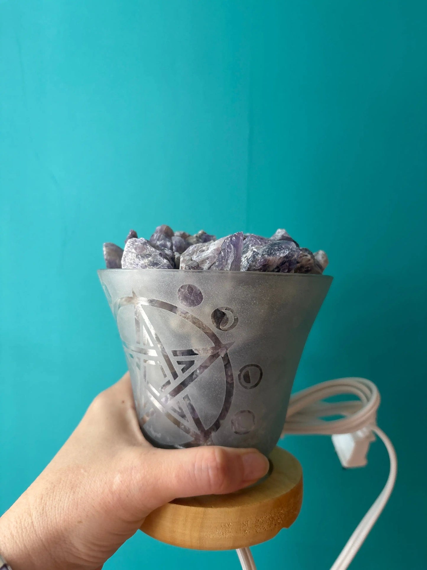 Amethyst lamp in frosted glass with natural amethyst crystals and wooden base held against blue background