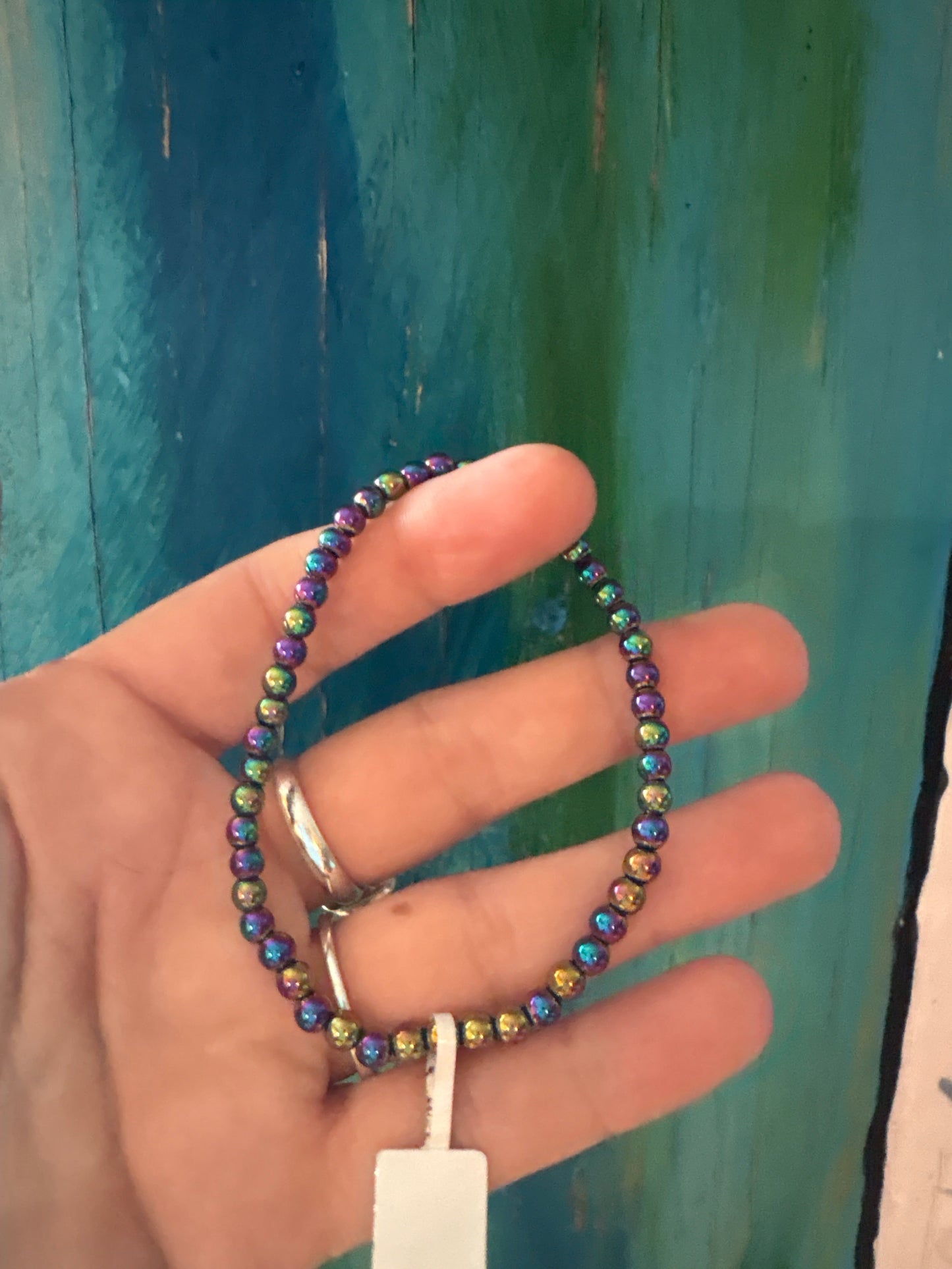 Hematite Rainbow Bracelet with 4mm iridescent beads held in hand against blue background