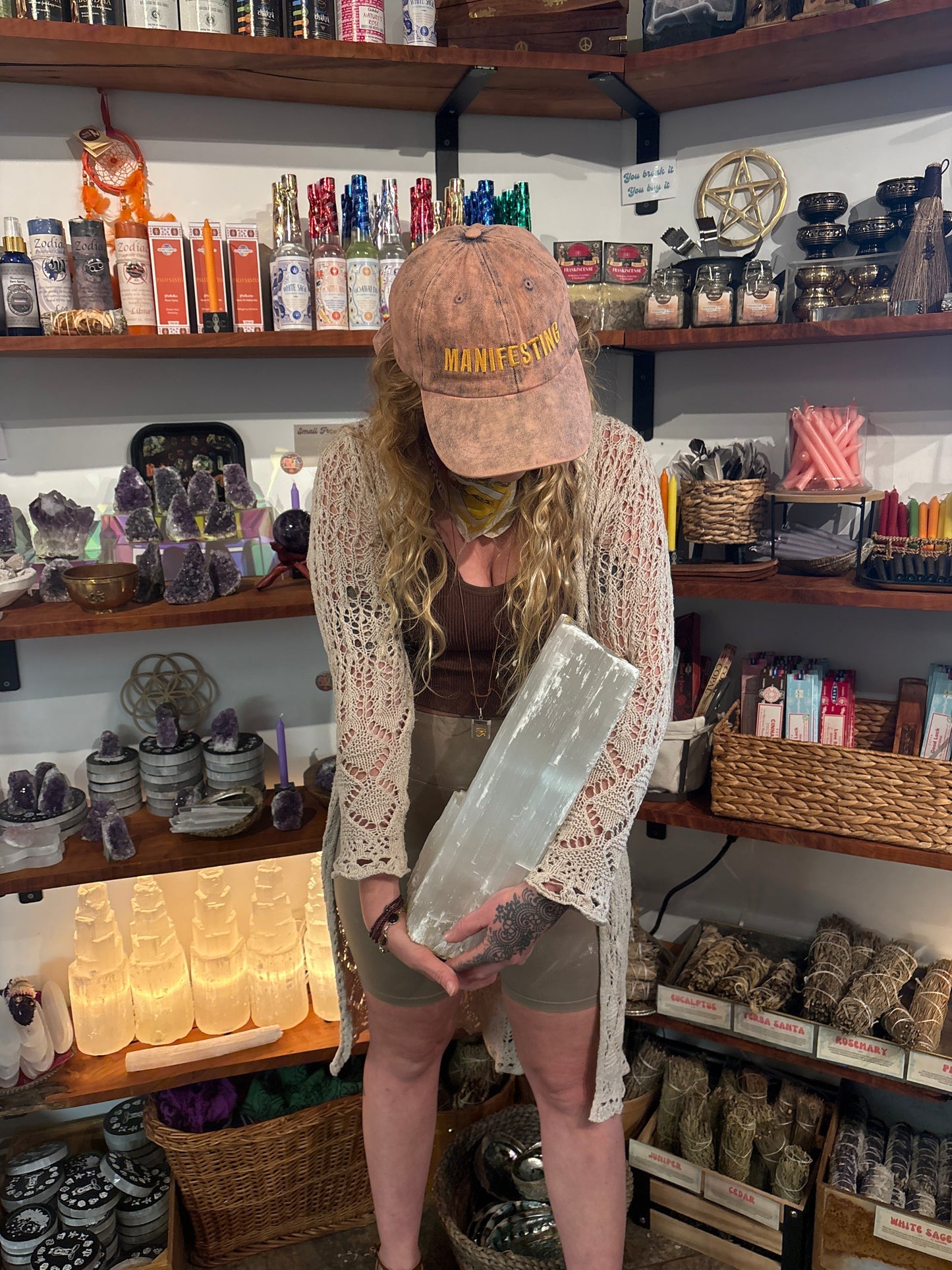 Woman holding large clear Selenite Log crystal in a spiritual shop with shelves of candles and crystals.