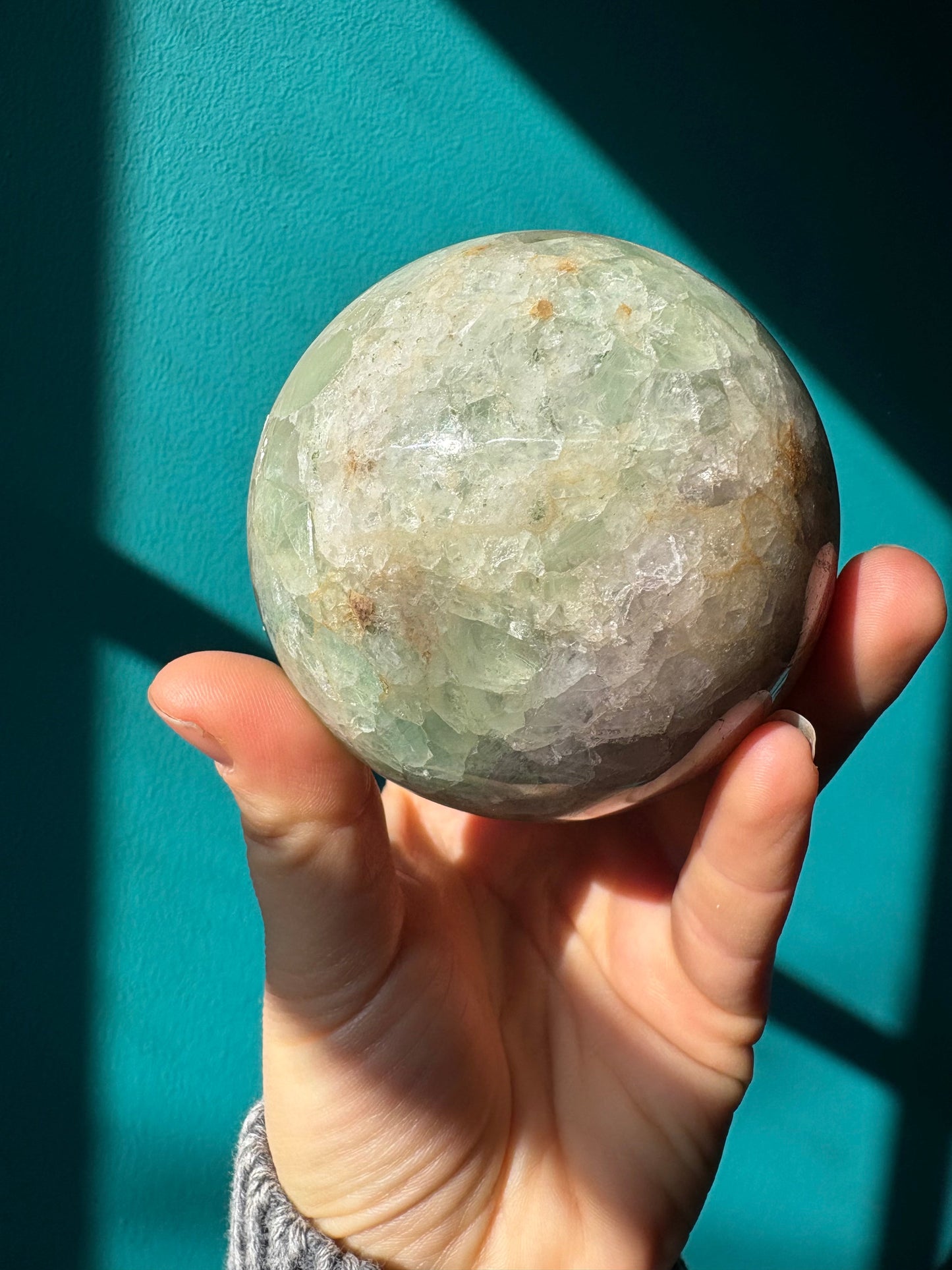 40mm fluorite sphere held in hand against teal background