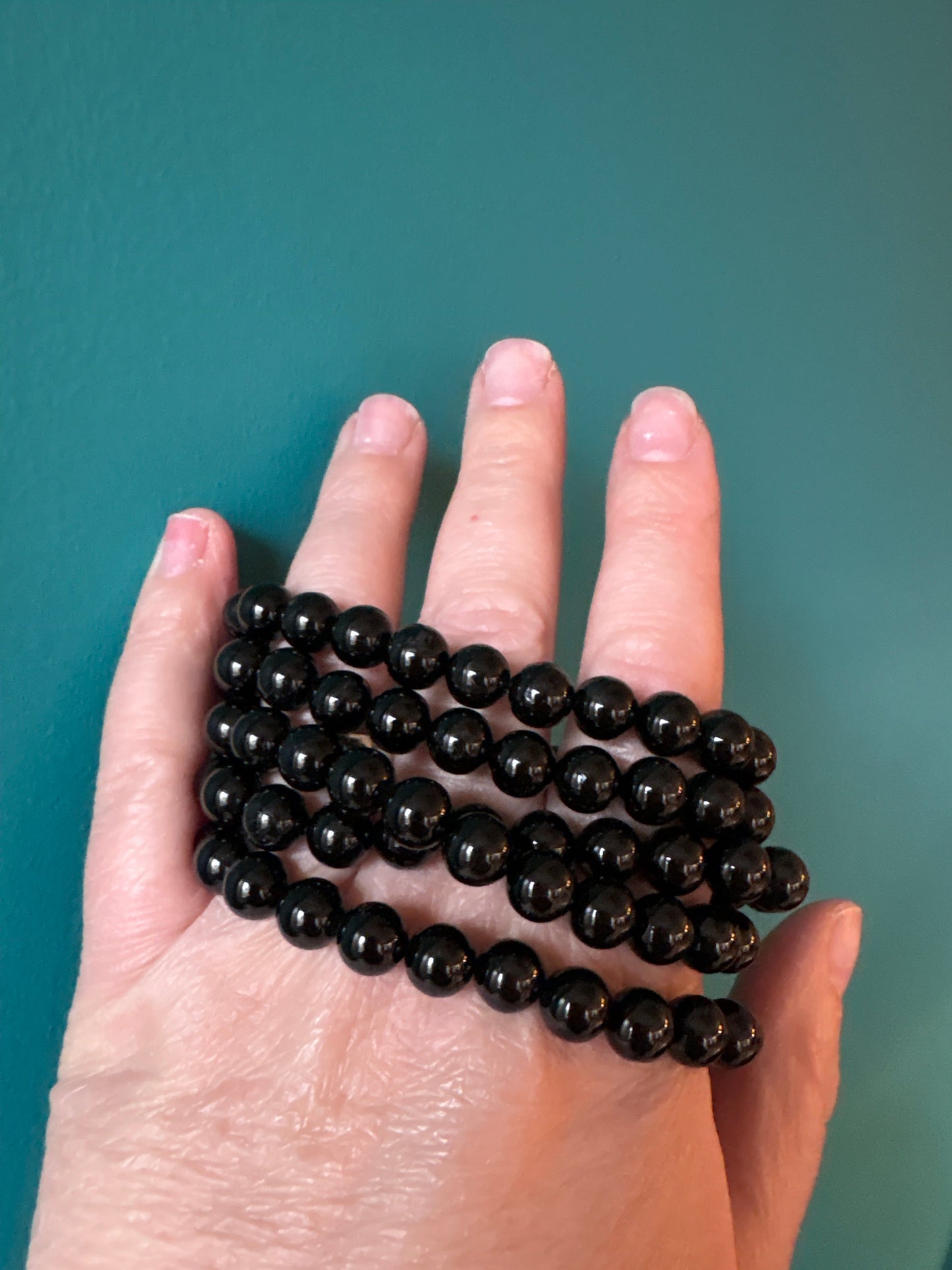 Black tourmaline bead bracelet held in hand on teal background