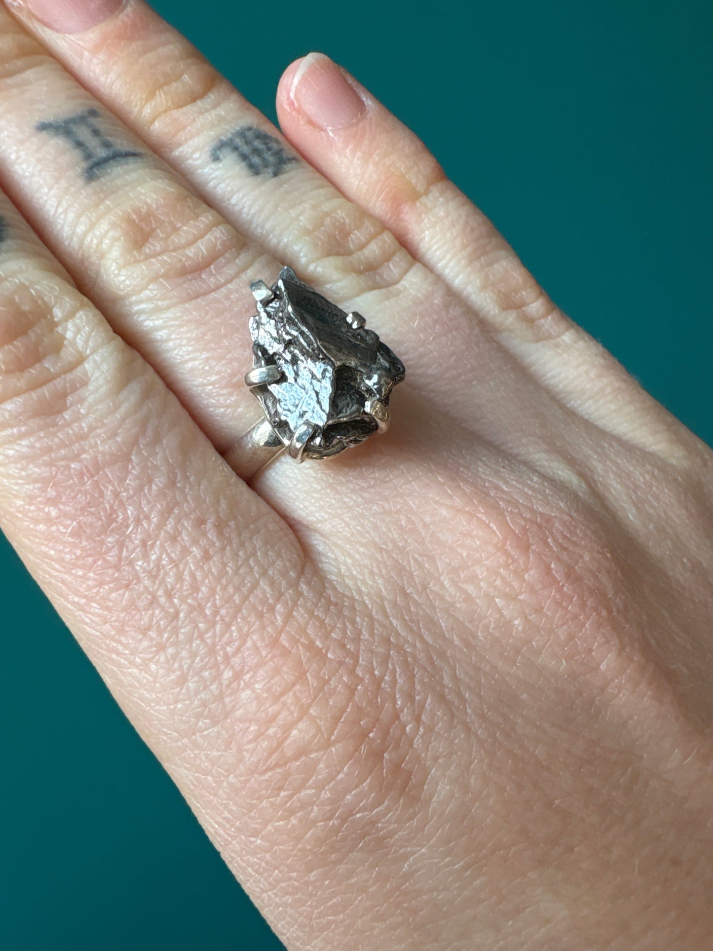 Close-up of a size 7 Ring Meteorite worn on finger against green background