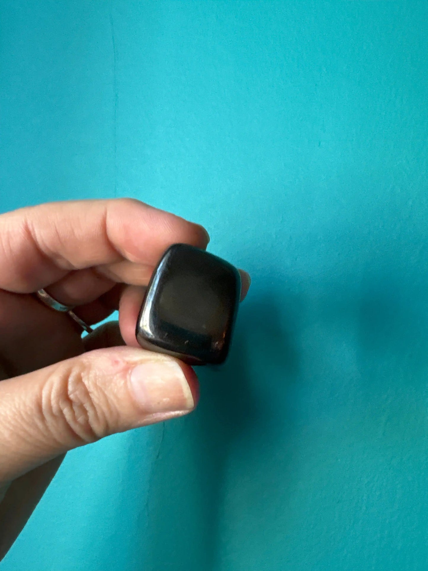 Hand holding a polished black Shungite Tumble stone against a blue background