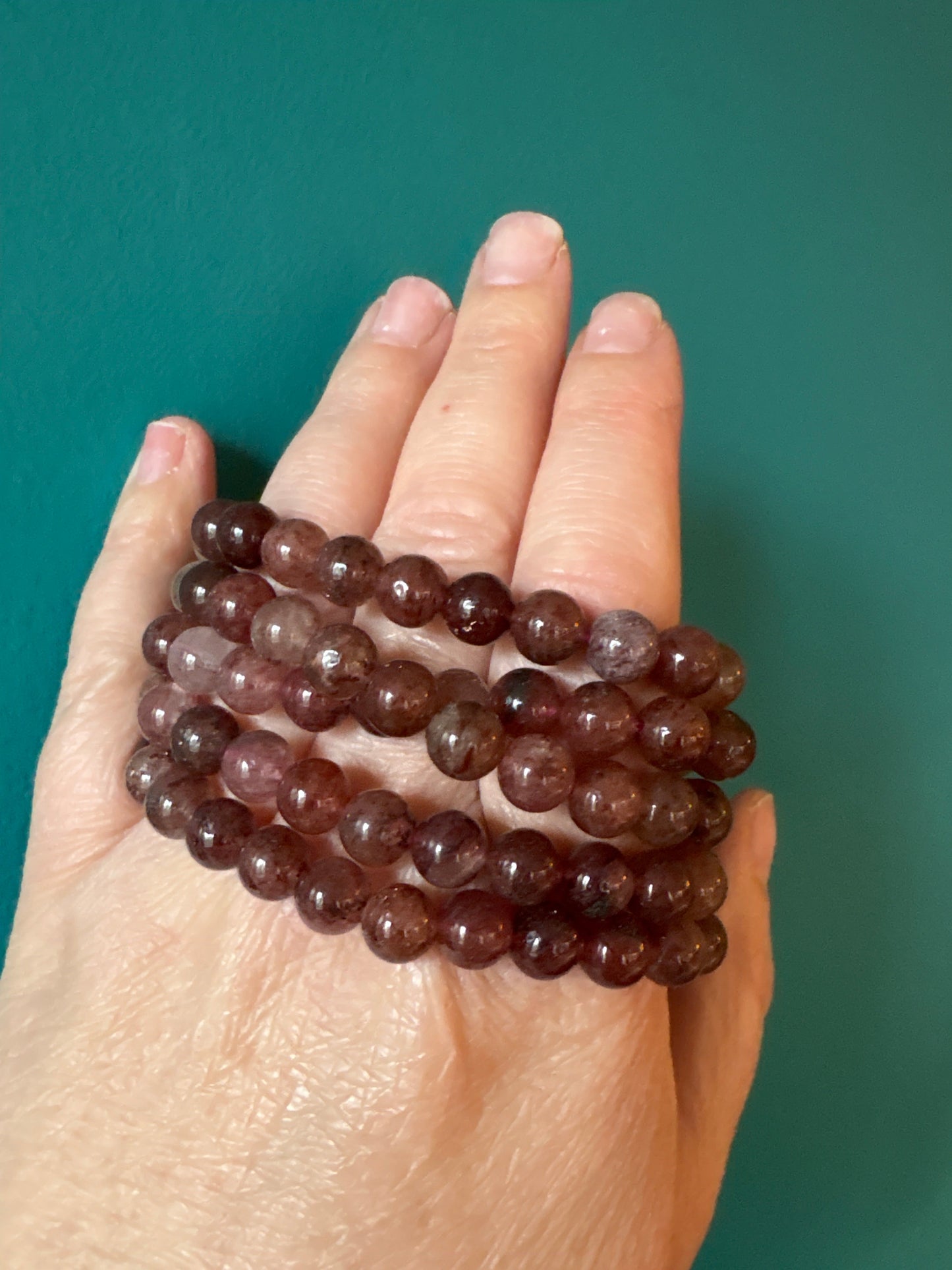 Bracelet Strawberry Quartz 8mm beads on hand against teal background, polished round stones, spiritual jewelry accessory