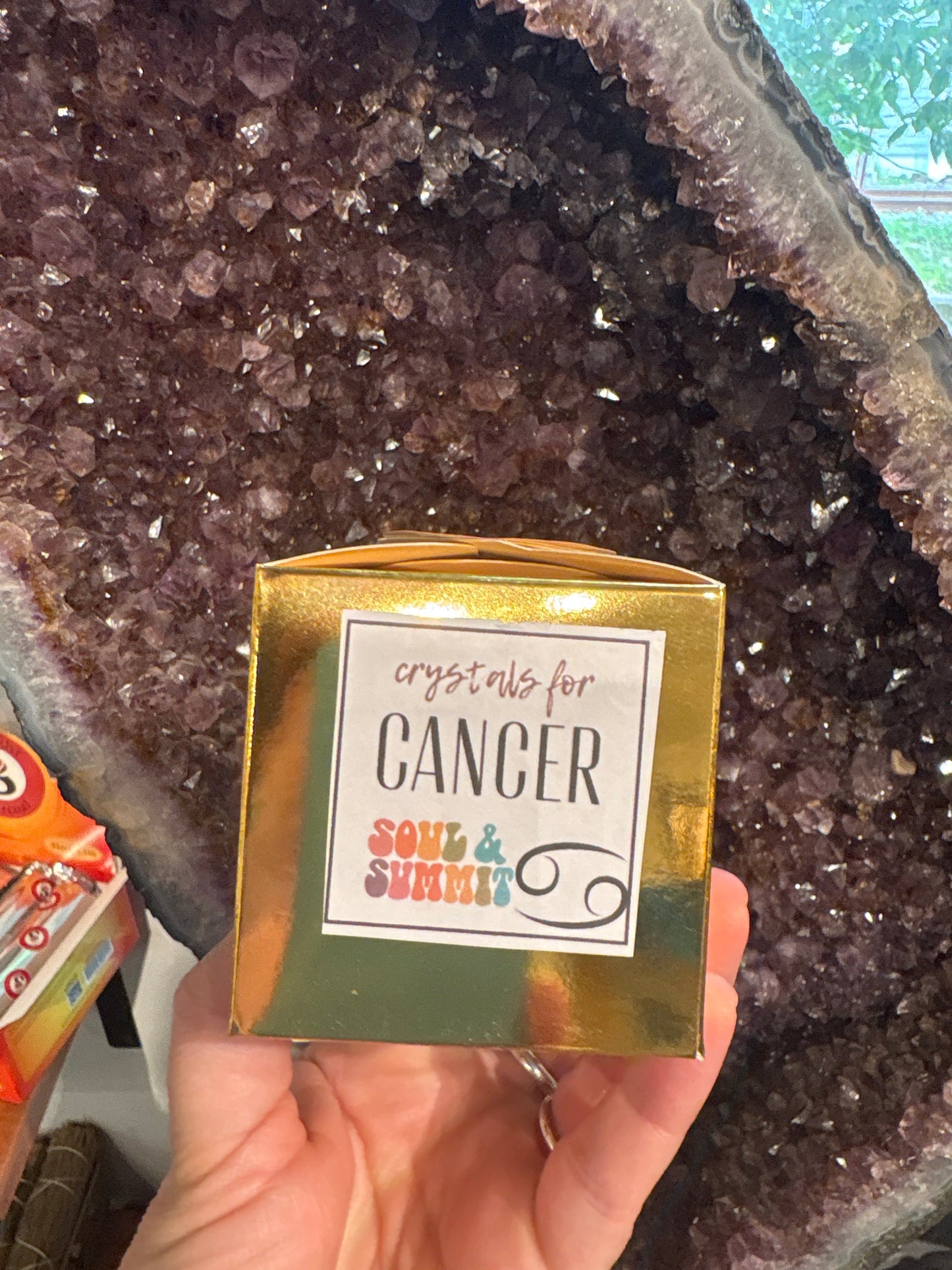 Cancer Crystal gift box with crystals for Cancers held in front of a large amethyst geode background