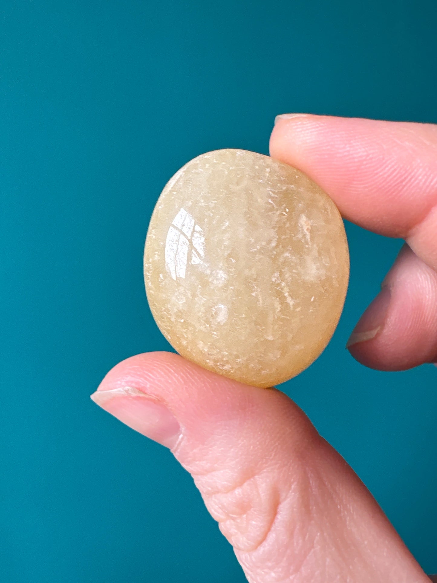 Hand holding a polished yellow aventurine tumble stone against a teal background