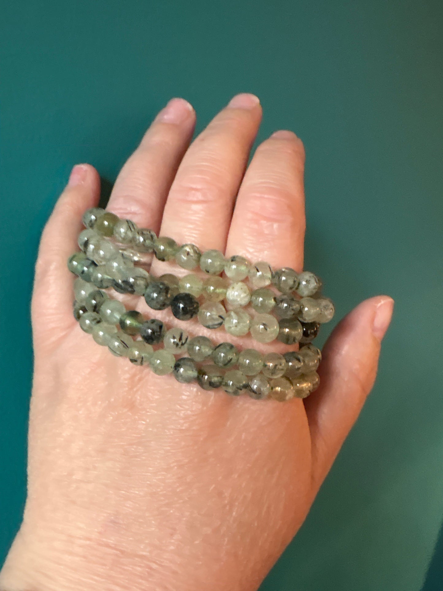 Bracelet Prehnite with 8mm translucent green beads worn on hand against teal background