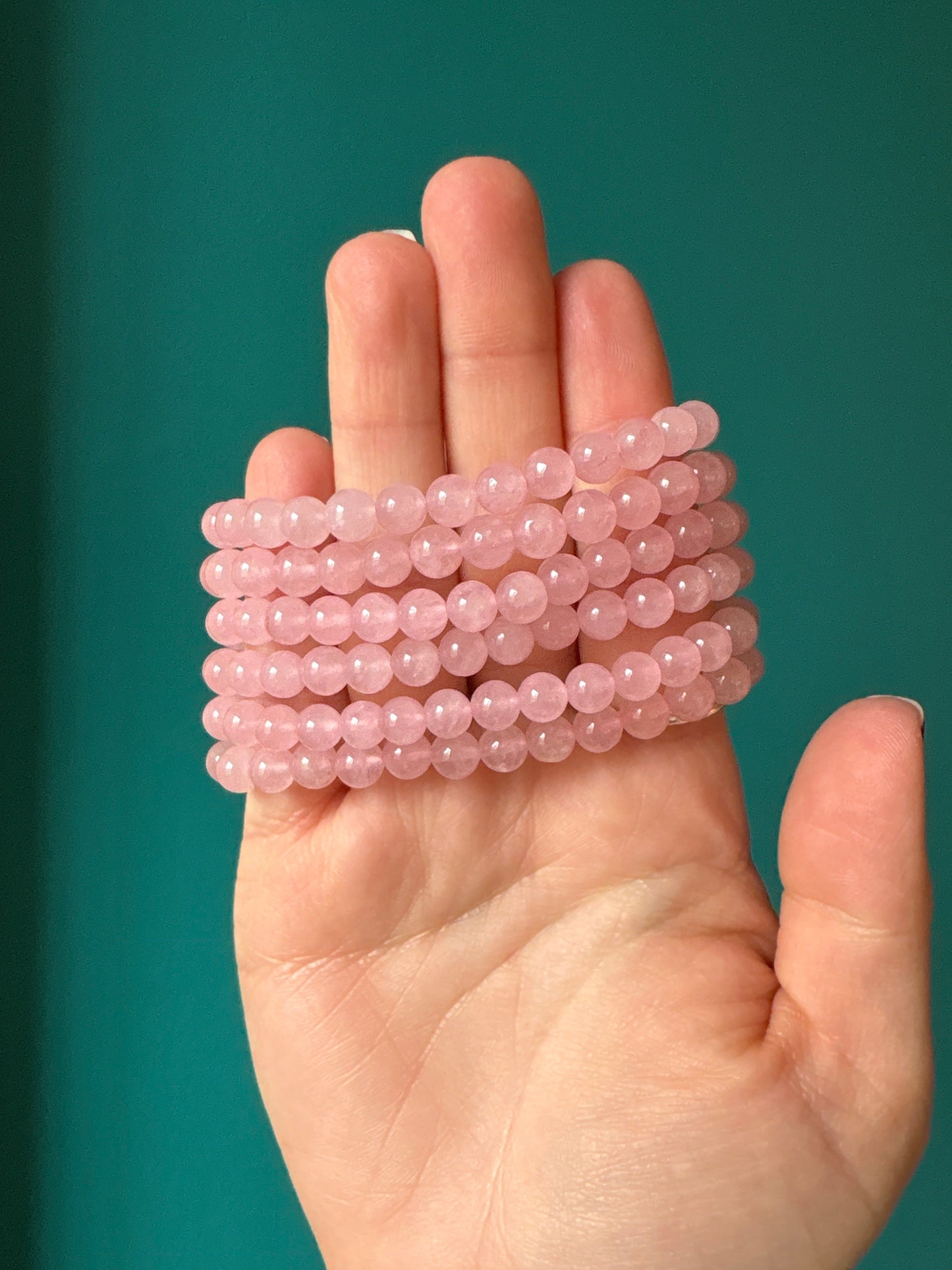 Close-up of a hand holding multiple strands of 6 mm Rose Quartz bead bracelets against a green background