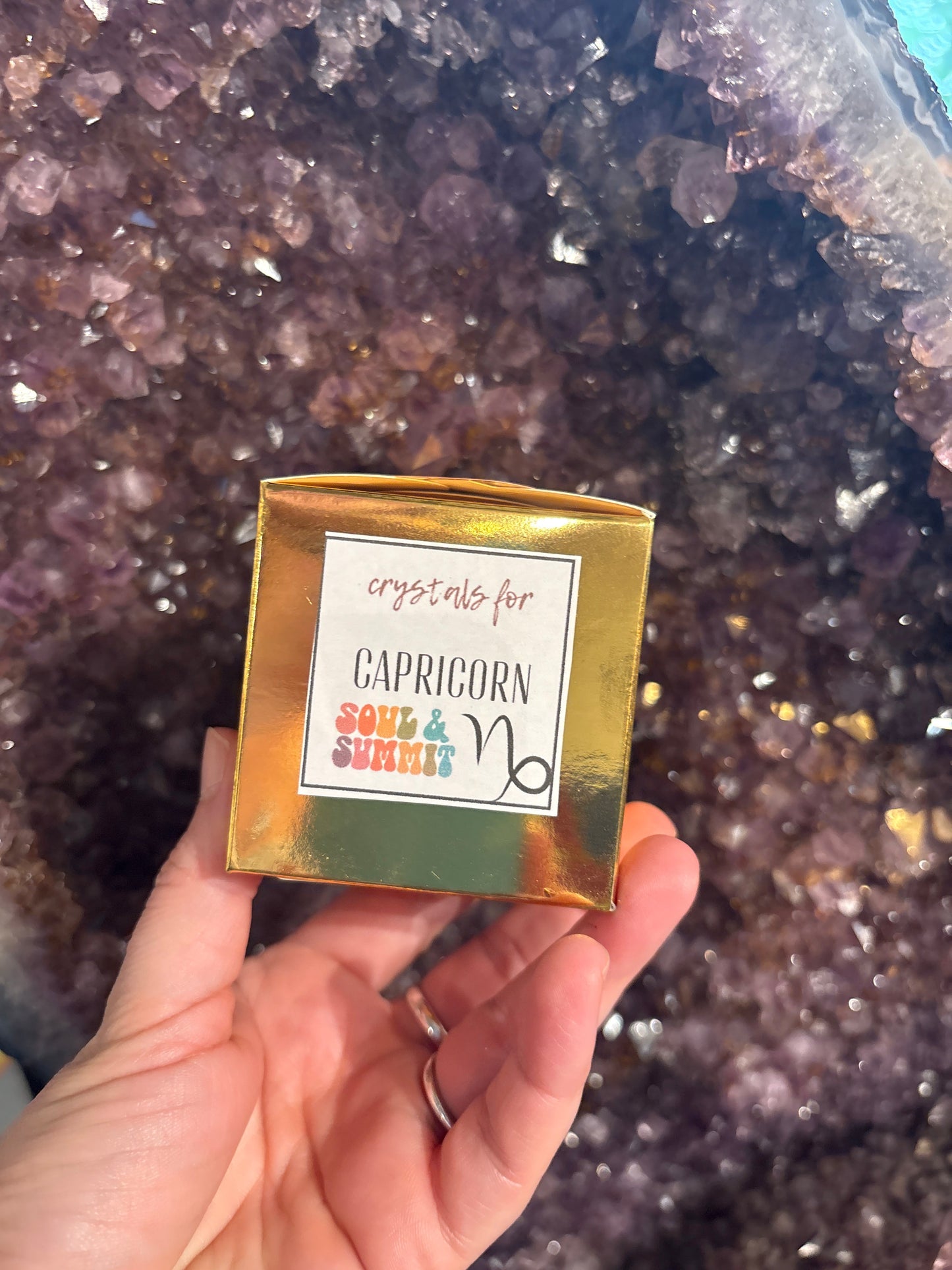 Hand holding a Capricorn Crystal Gift Box with crystals in the background