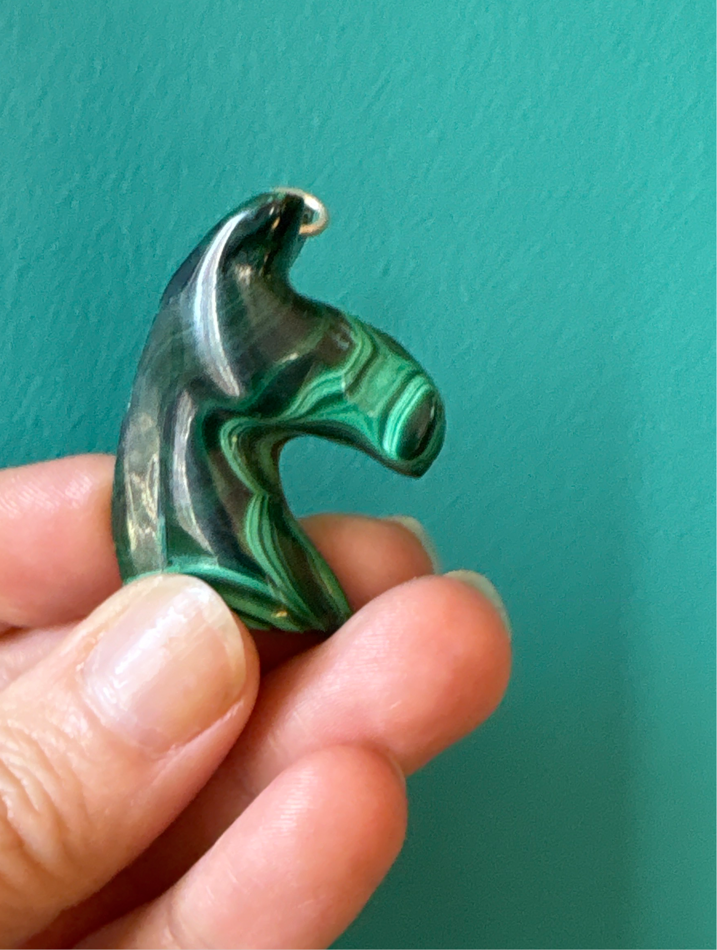 Hand holding green Malachite Horse Pendant with healing properties against teal background