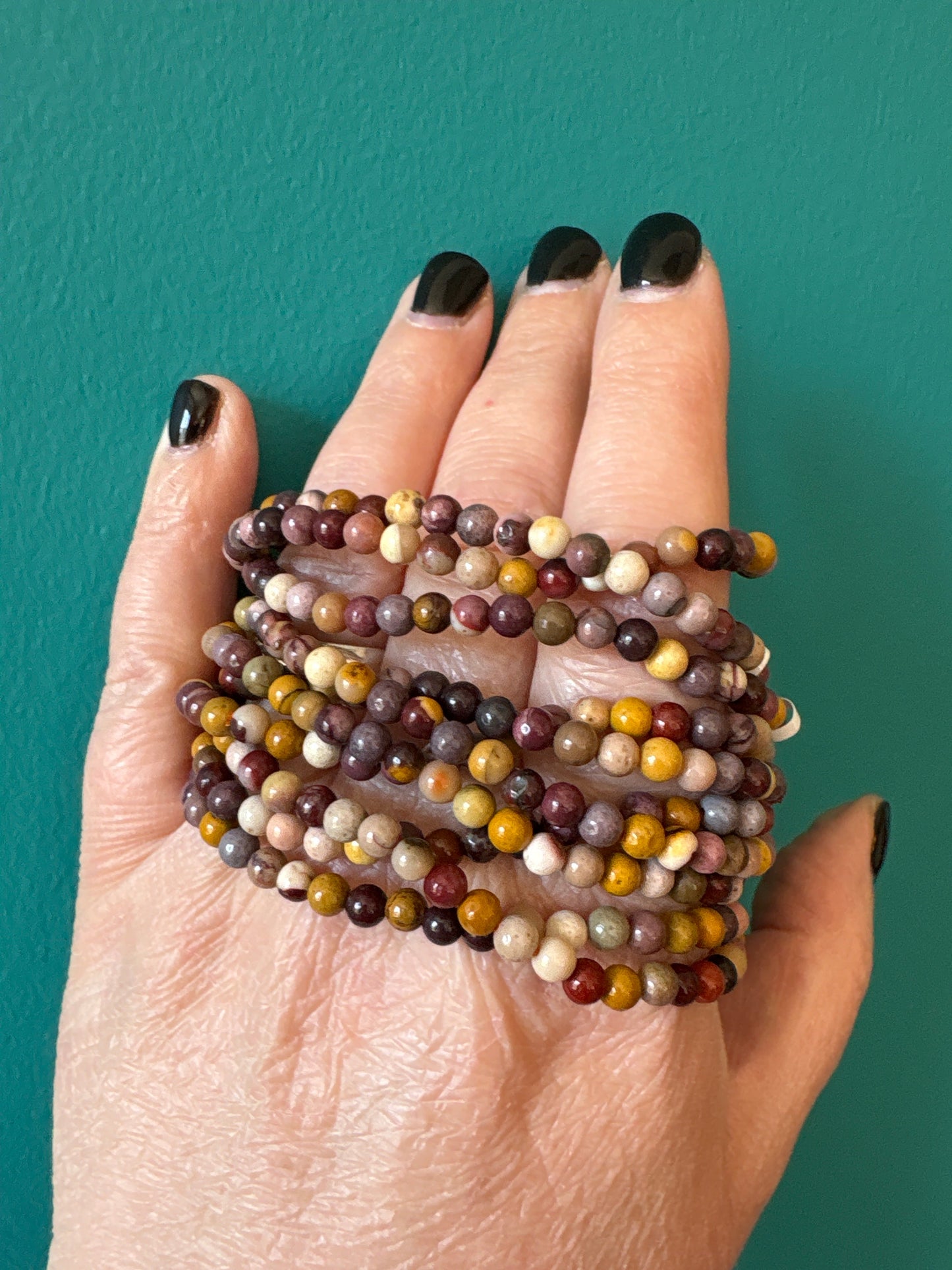 Bracelet Mookaite with 4mm multicolored beads worn on hand against teal background