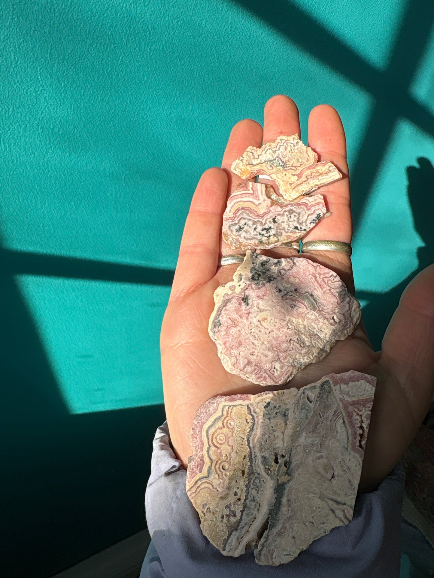 Hand holding Rhodochrosite slab gemstones with pink and red patterns against teal background