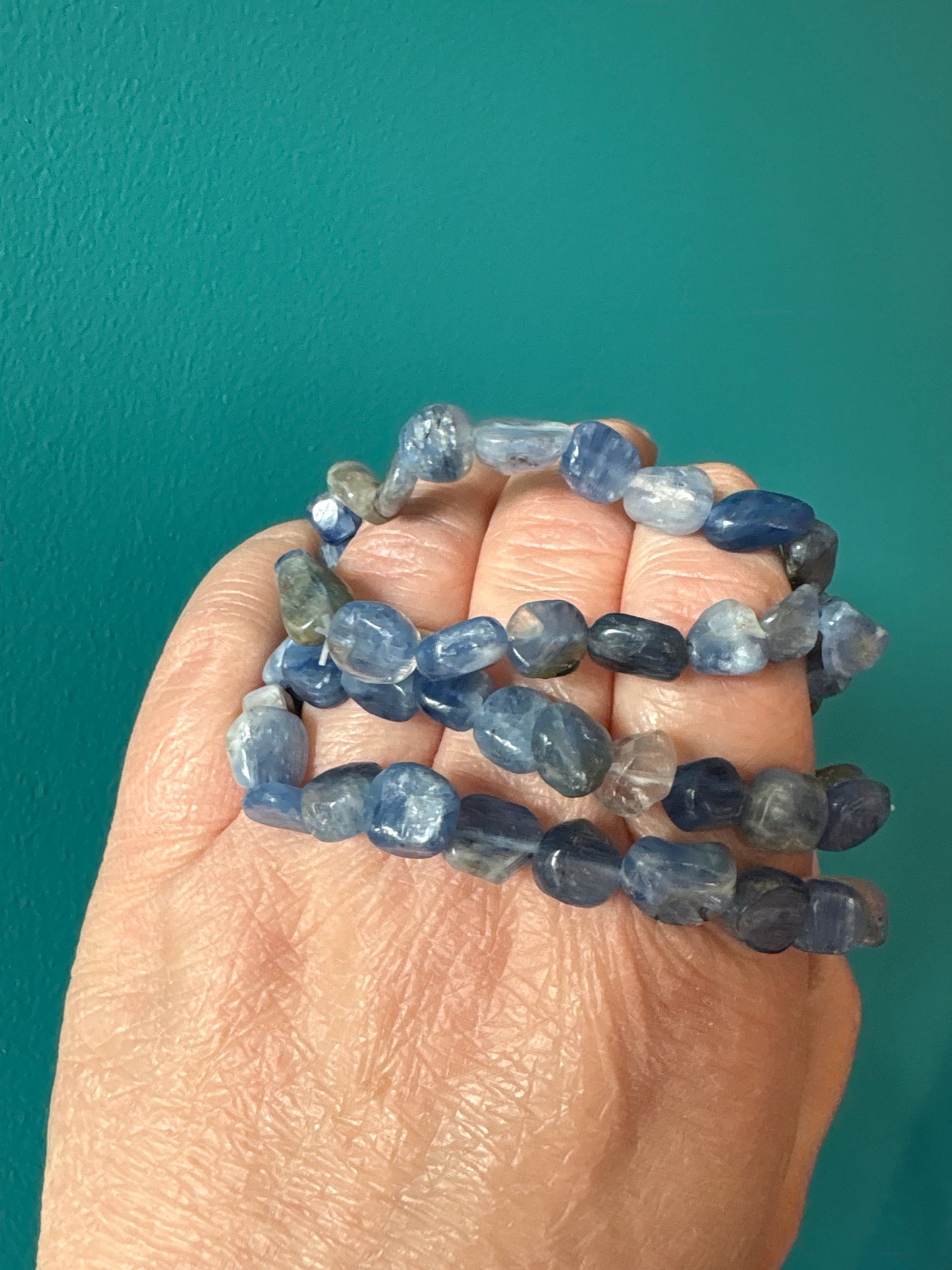Kyanite tumble stone bracelet with 8-10mm polished blue beads on hand against teal background