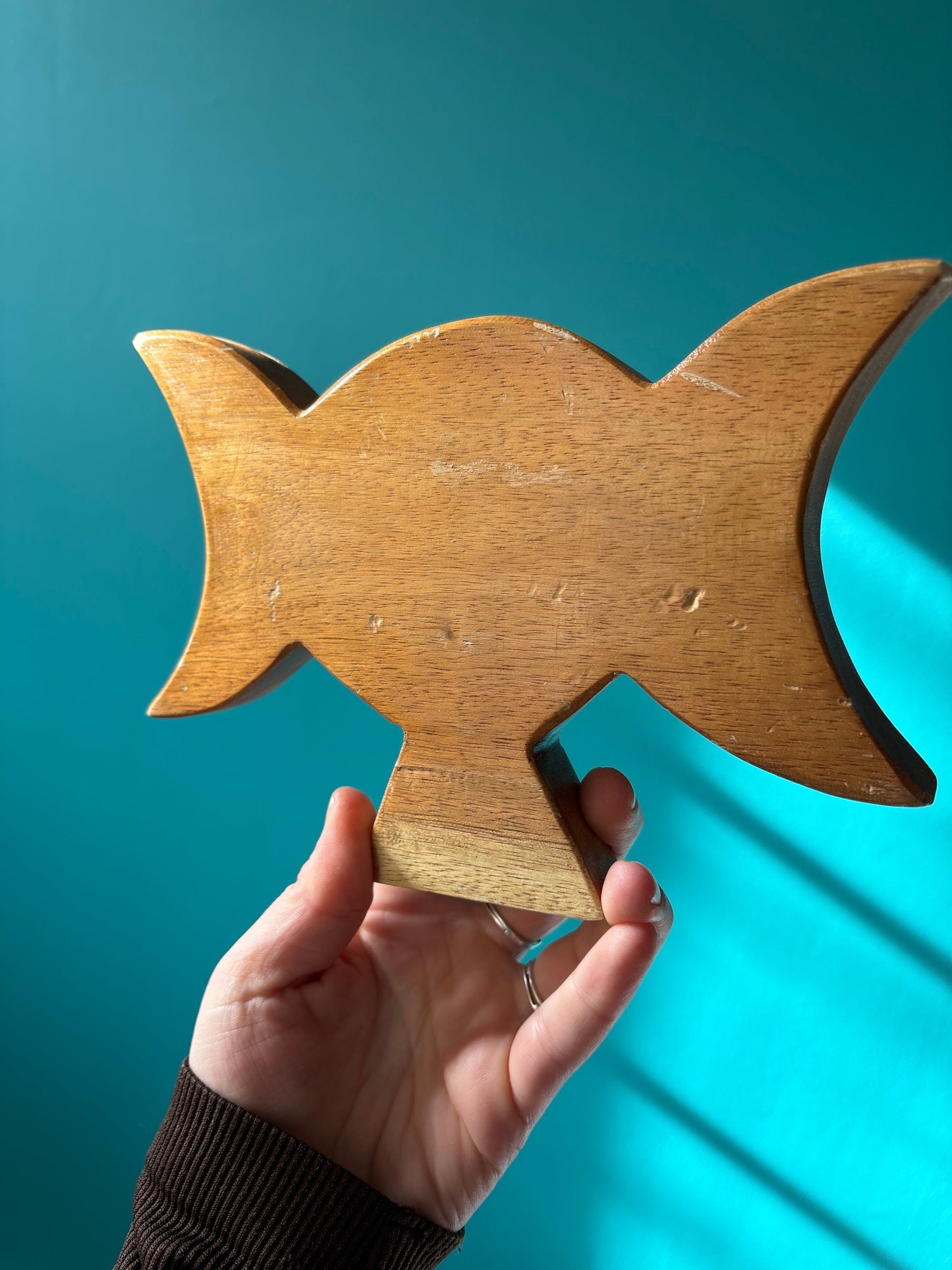 Hand holding a wooden Triple Goddess Altar Statue against a teal background