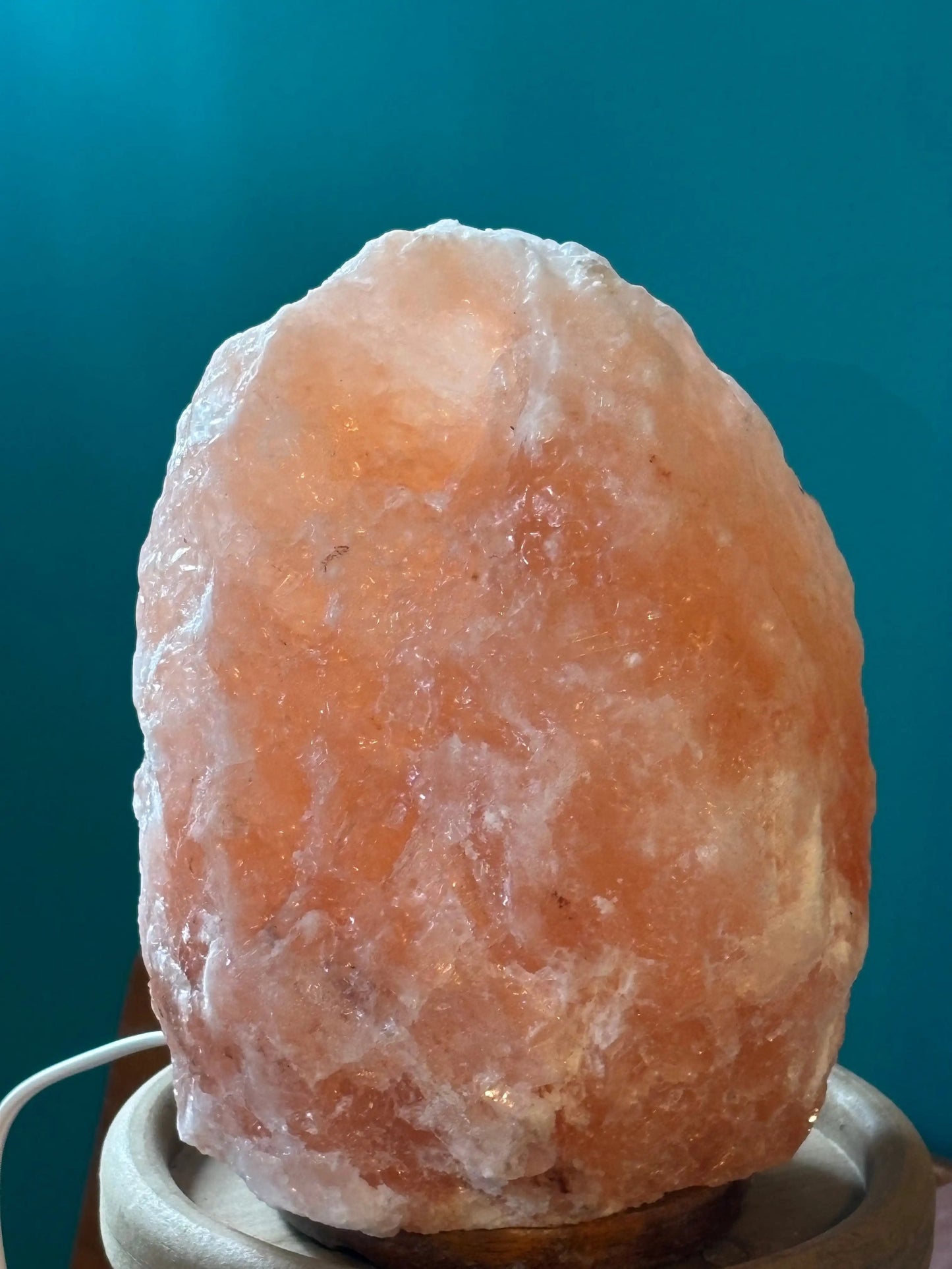 Pink Himalayan Salt Lamp emitting warm glow on wooden base with cord against blue background