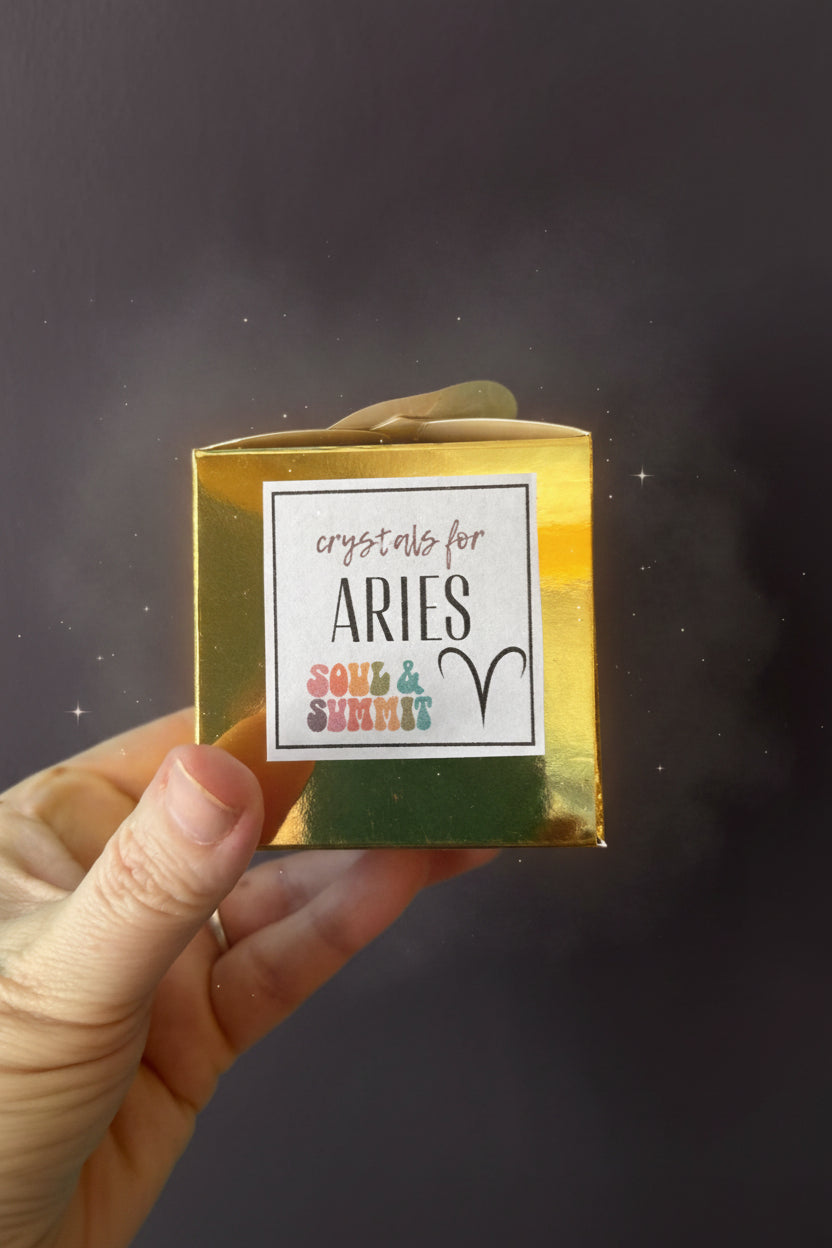 Hand holding gold Aries Zodiac Gift Box with crystals for Aries label against teal background