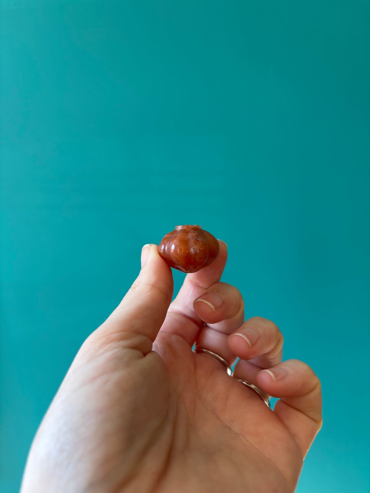 Hand holding small orange calcite Halloween pumpkin carving against teal background