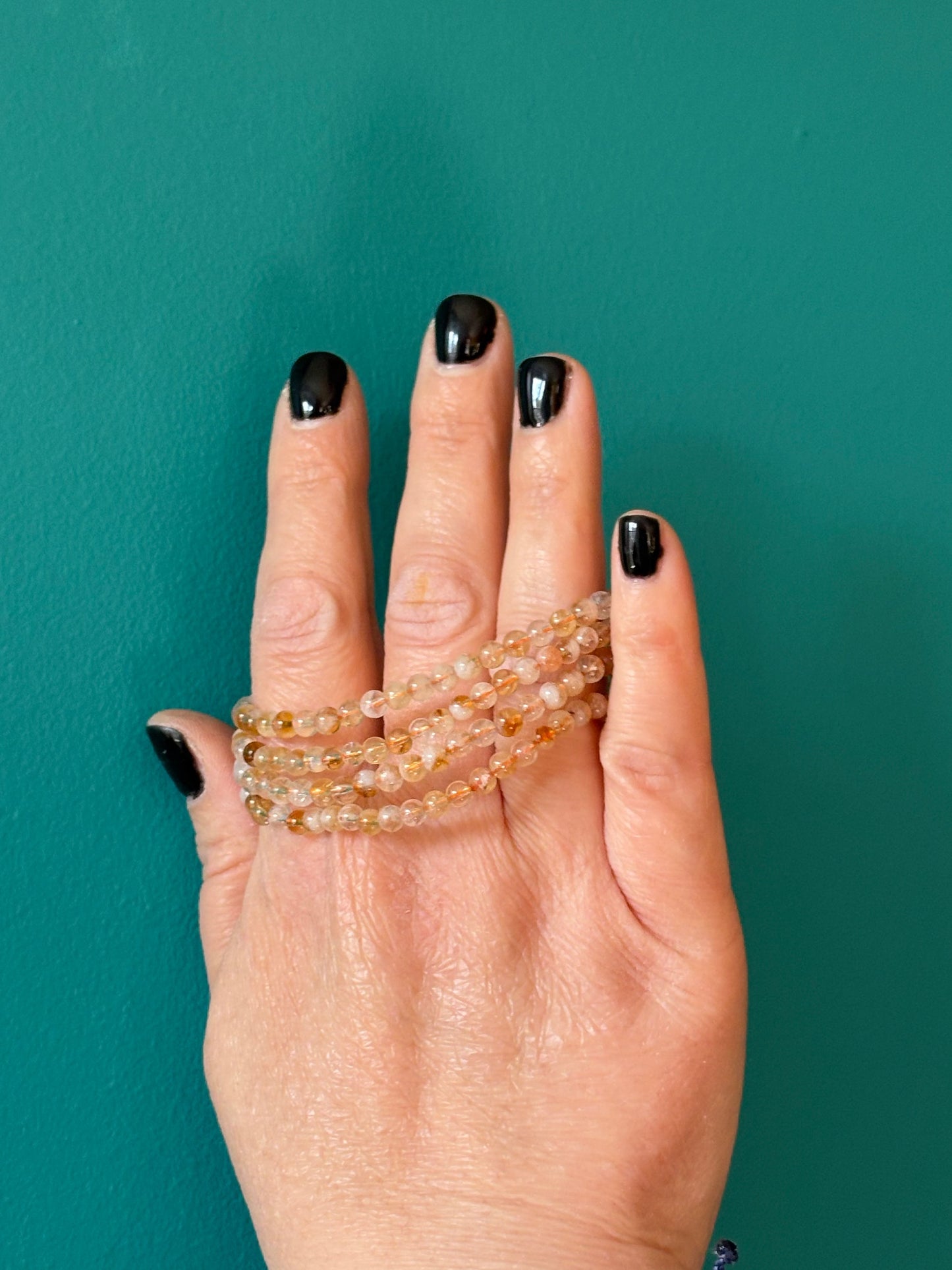 Citrine bracelet with 4mm genuine Citrine stones worn on hand with black nail polish against teal background