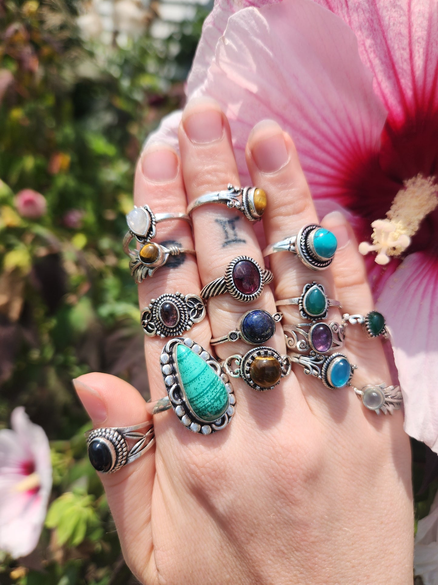 Hand wearing multiple sterling silver rings with various colorful stones against floral background