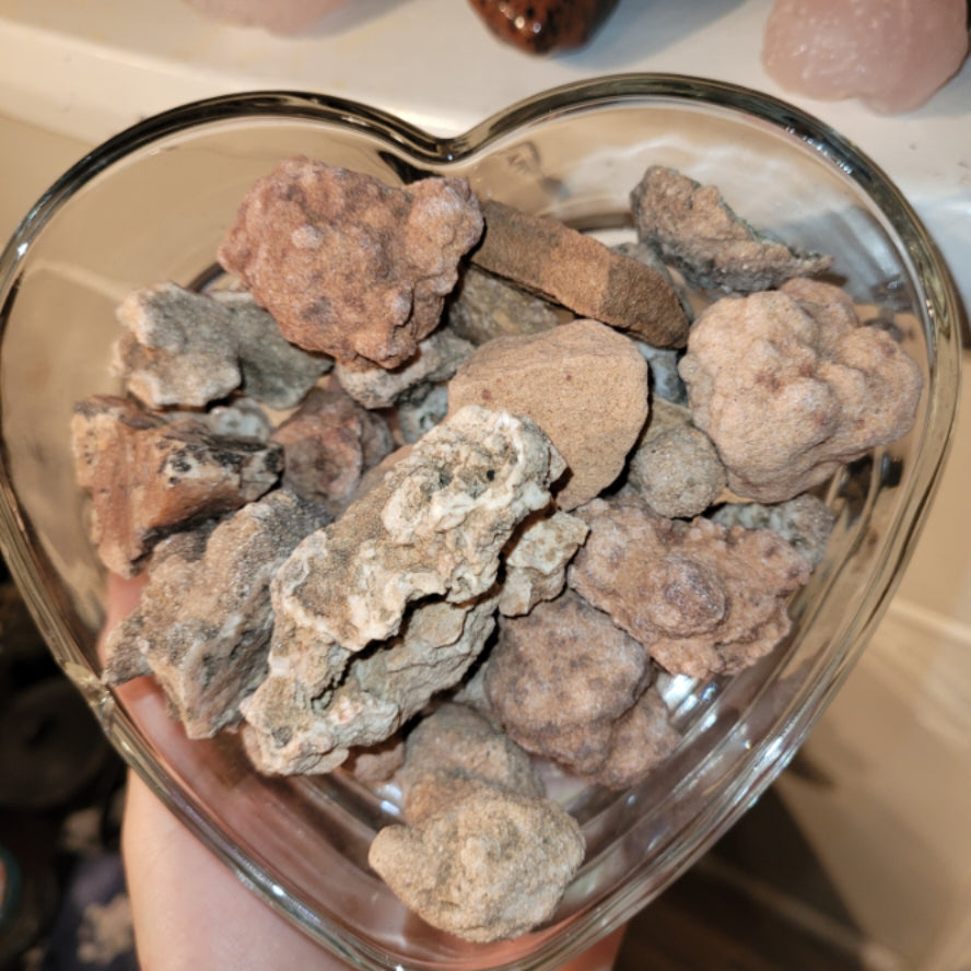 Heart-shaped glass bowl filled with raw Arizona chalcedony stones mined in Arizona by Syd, showcasing natural earthy patterns and colors.
