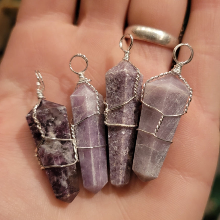 Hand holding four wrapped lepidolite pendants with silver wire, showcasing polished purple stones for healing and relaxation.