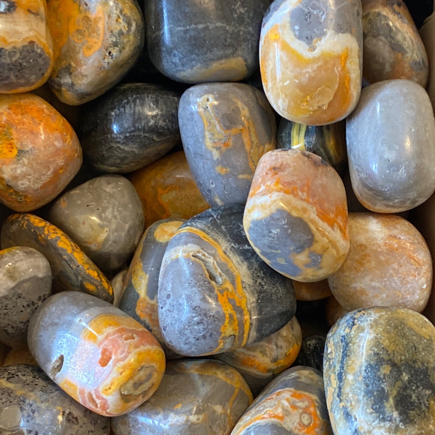 Close-up of polished Bumblebee Jasper Tumble stones with vibrant yellow, orange, gray, and black patterns.