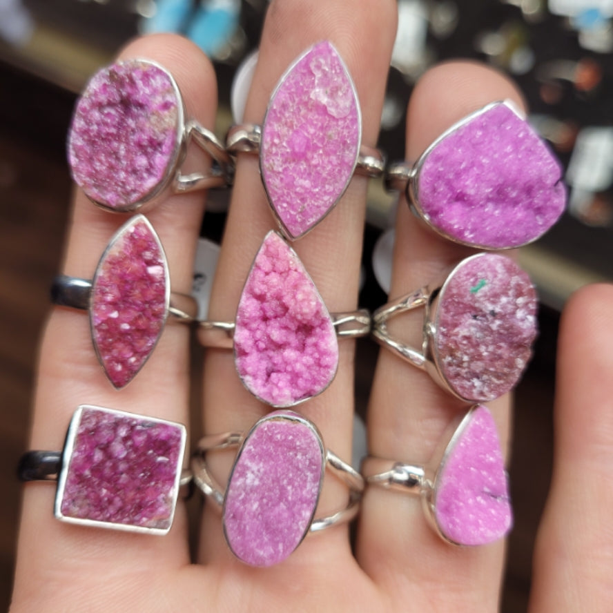 Collection of pink ring cobalto calcite druzy gemstones with silver bands on fingers