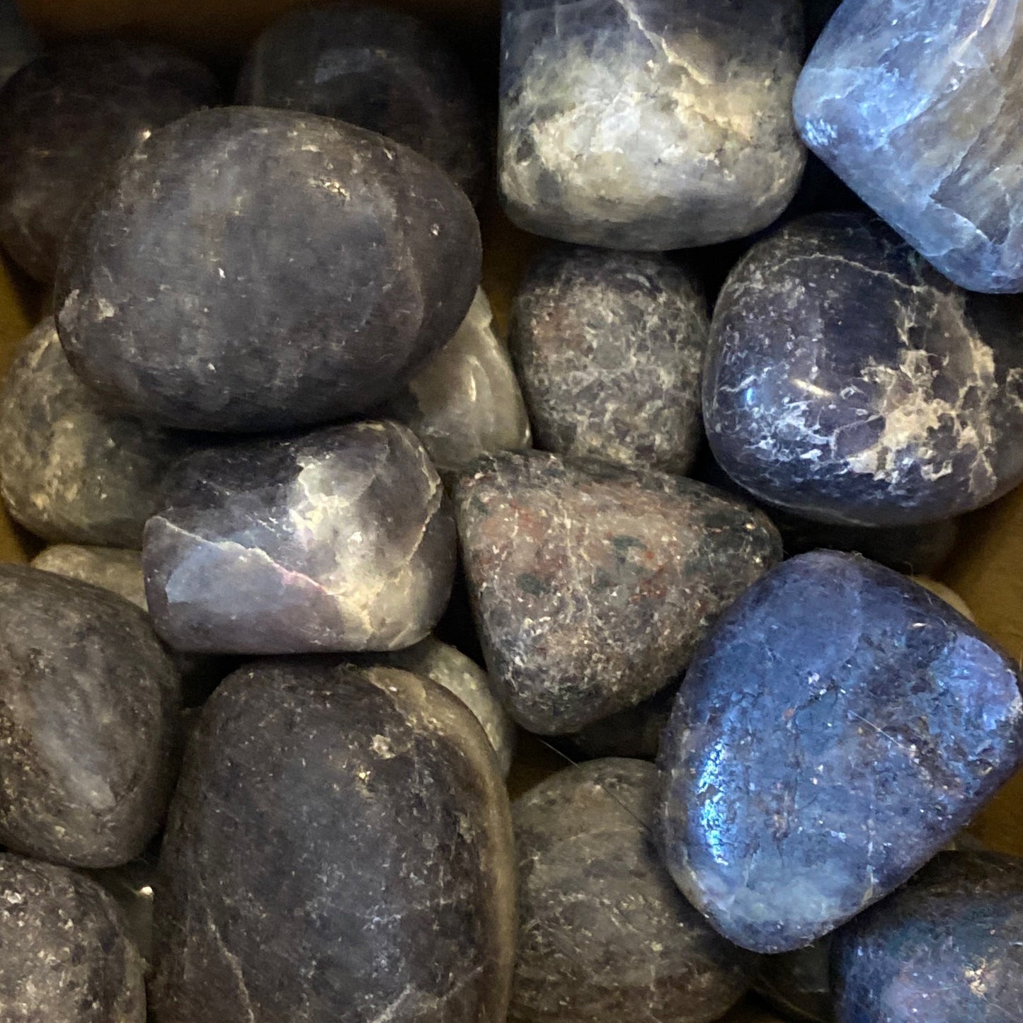Pile of polished deep blue iolite tumbles with smooth surfaces and natural variations