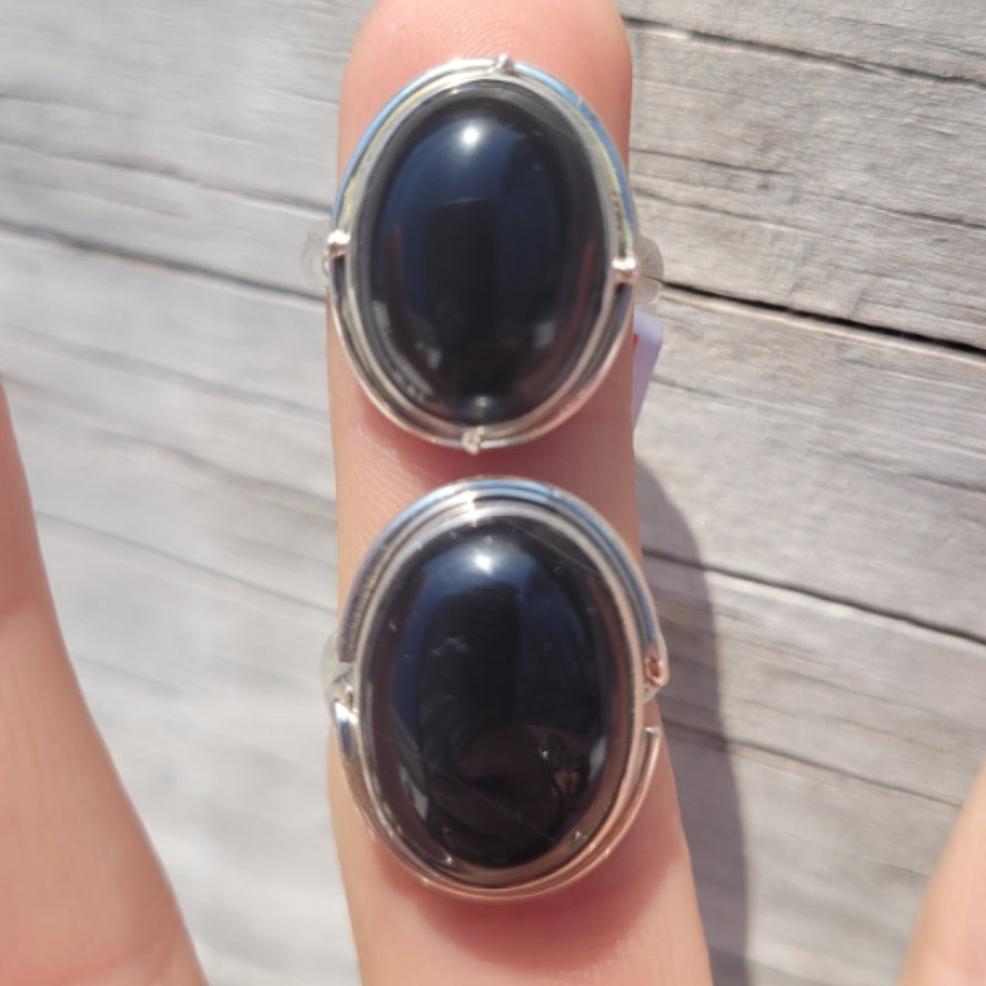 Obsidian rings in sizes 6 and 7 with polished black oval stones and silver bands on fingers