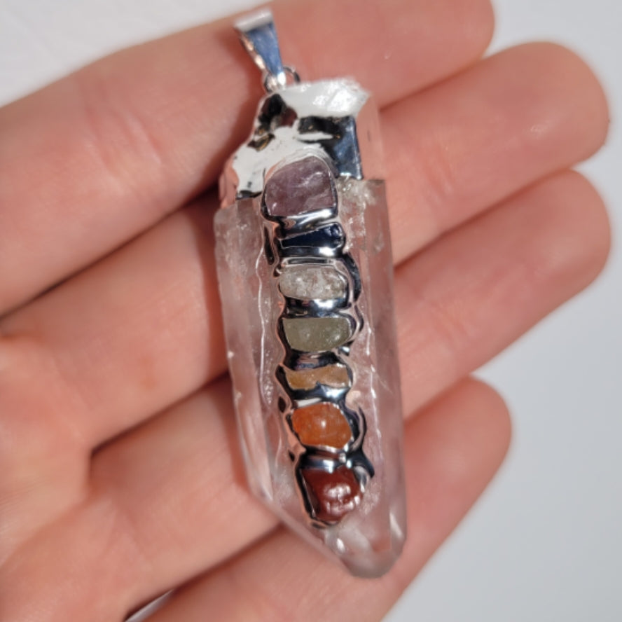 Clear quartz rough chakra pendant with seven colorful chakra stones held in hand