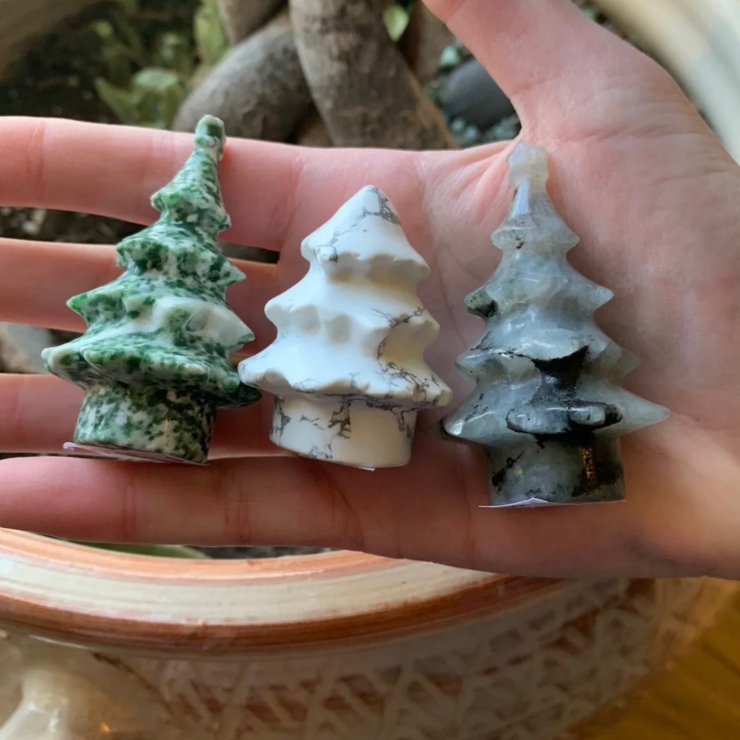 Hand holding three small crystal Christmas trees in green, white, and gray colors for festive holiday decor
