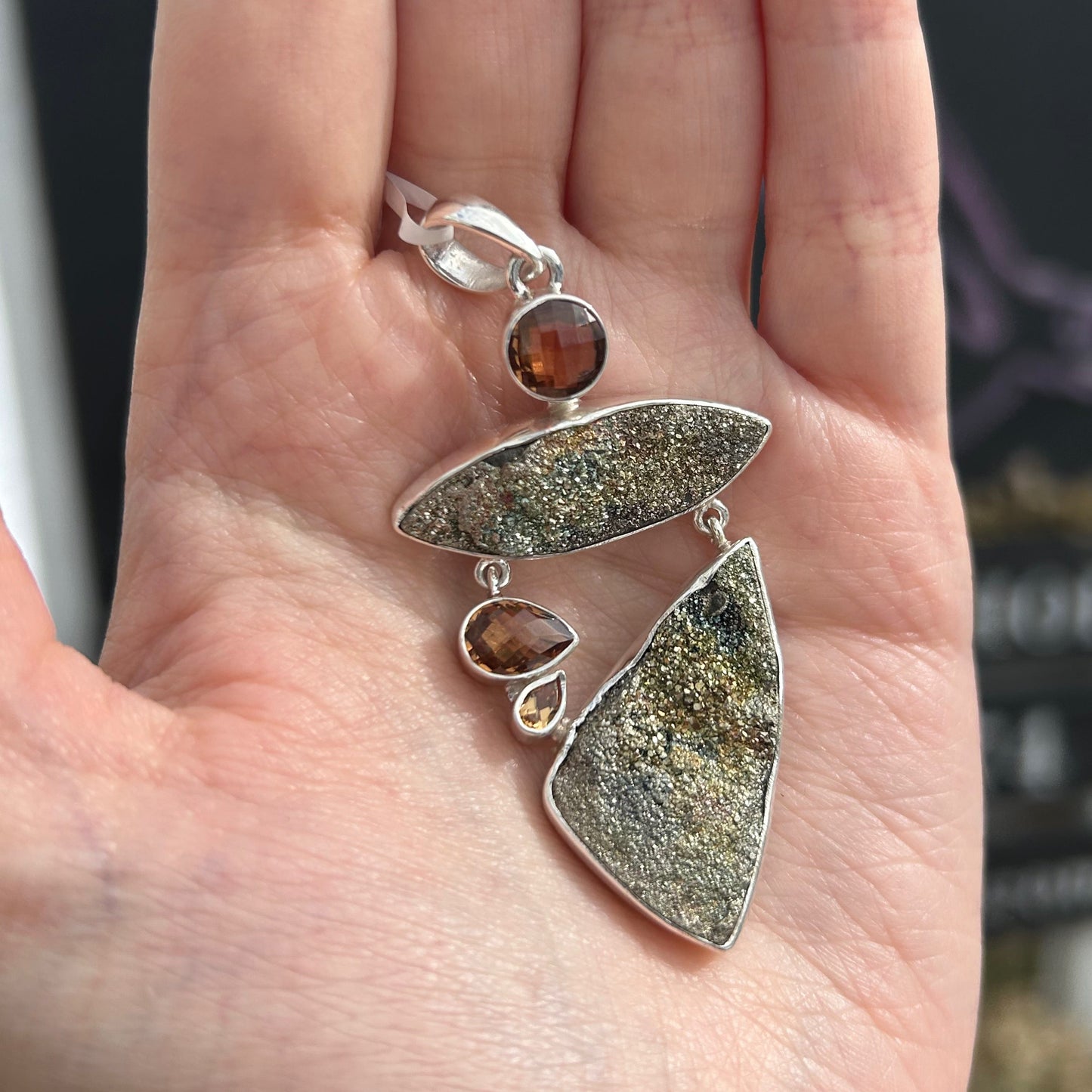 Spectropyrite druzy pendant with faceted brown gemstones held in hand