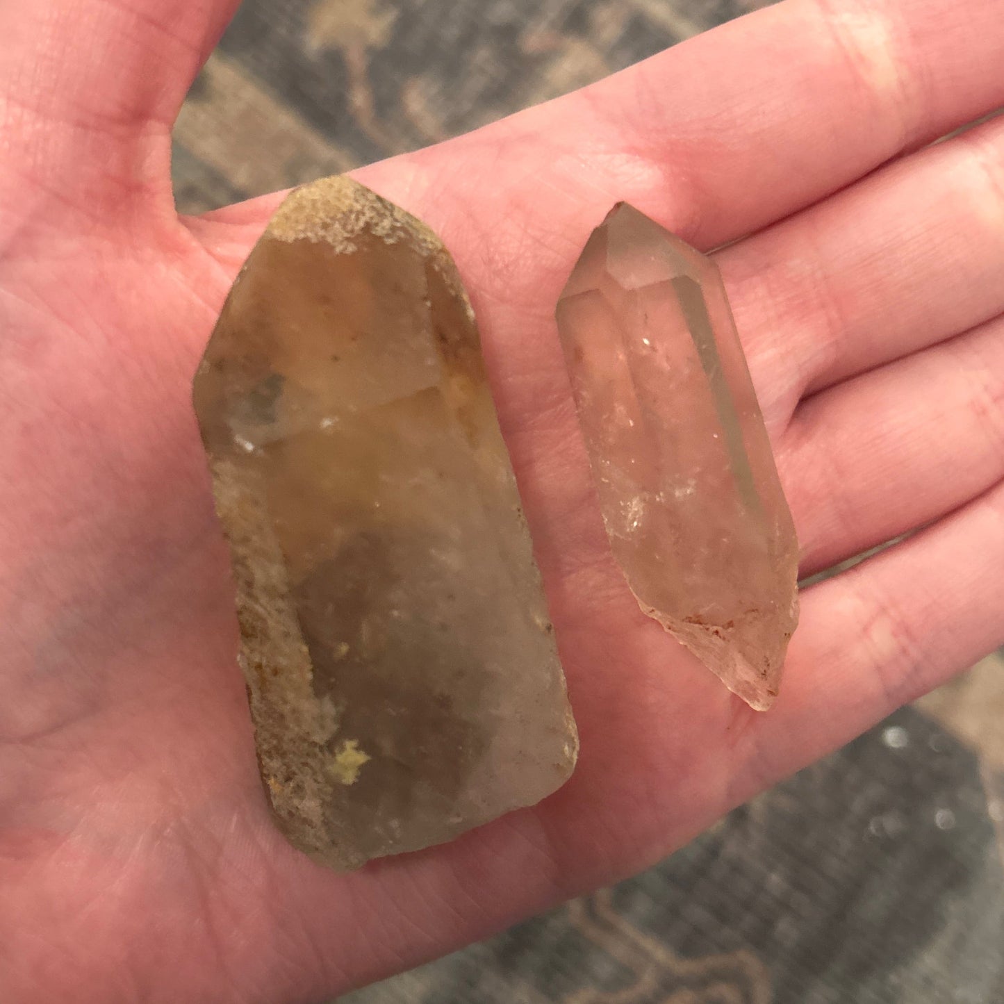 Two smokey quartz crystals with visible natural inclusions held in a hand against a blurred background