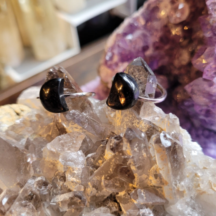 Ring Rainbow Obsidian Moon featuring a black crescent-shaped obsidian stone set on a silver band displayed on clear quartz crystals