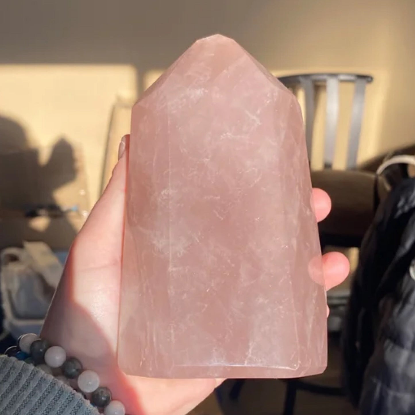 Hand holding a polished lavender rose quartz tower crystal in soft natural light
