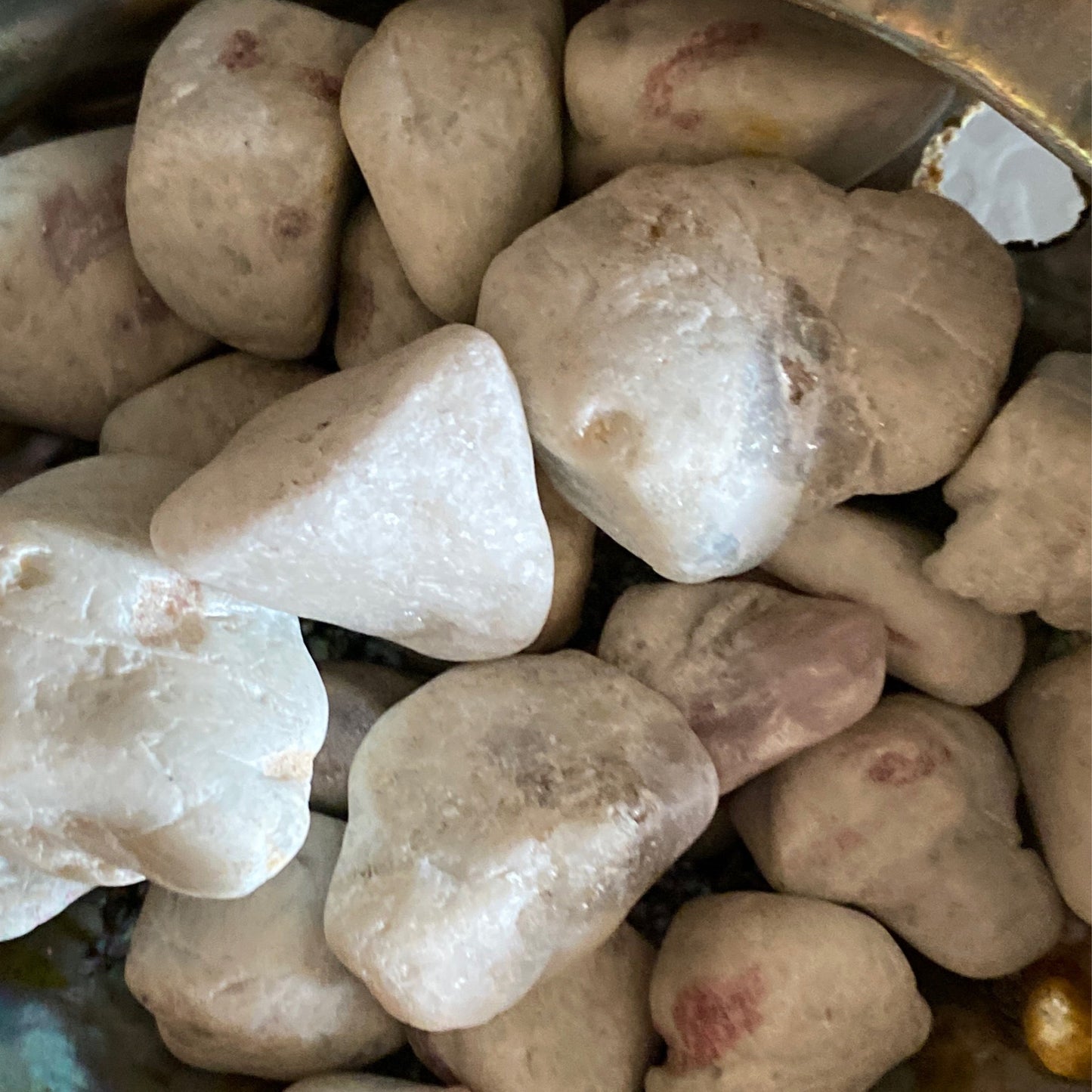 close-up of pale white and light pink tumble rubilite gemstones with smooth surfaces in a container