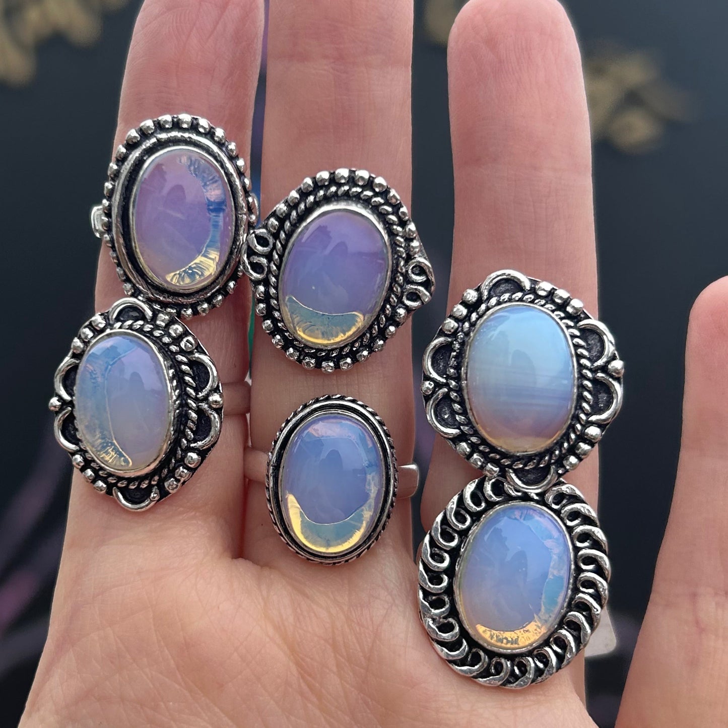 Five silver plated Opalite rings with intricate designs displayed on a hand