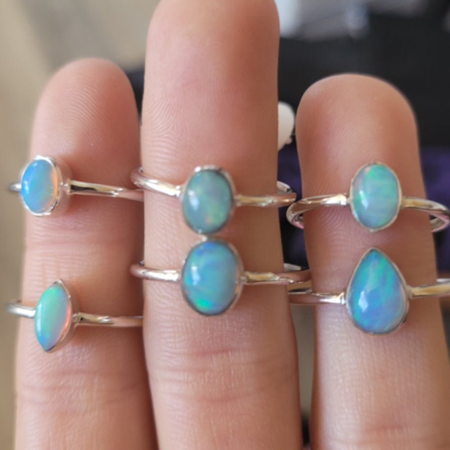 Close-up of fingers wearing multiple silver rings with Ethiopian opal gemstones in various shapes