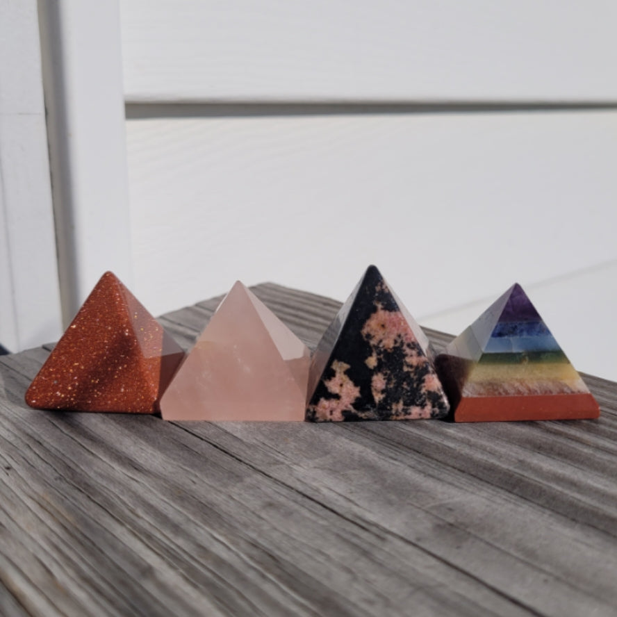 Set of colorful crystal pyramids including a Rhodonite pyramid on wooden surface