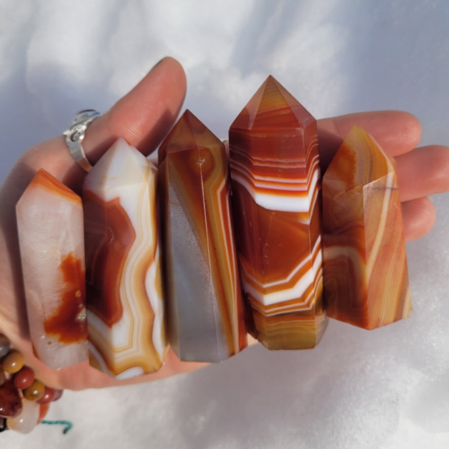 Hand holding multiple polished Carnelian Towers with distinct orange and white banding patterns against a soft background