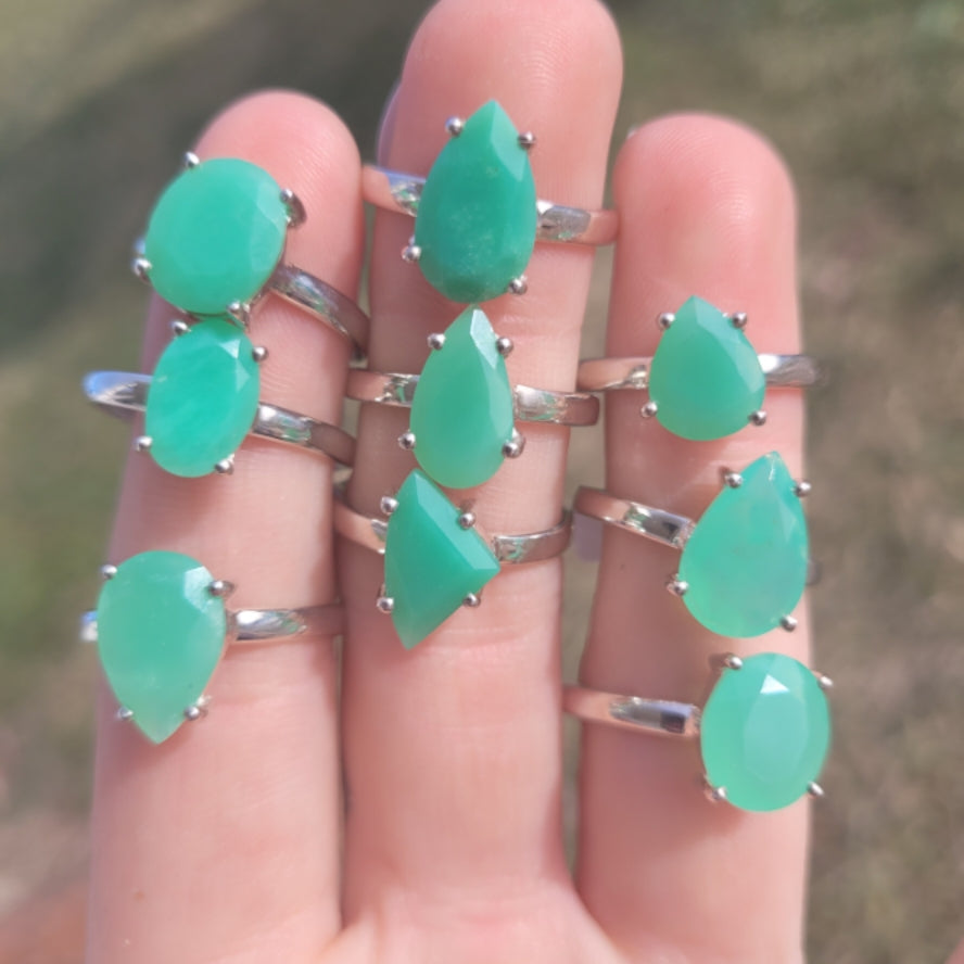 Collection of faceted chrysoprase rings with various green gemstone shapes on silver bands displayed on fingers outdoors