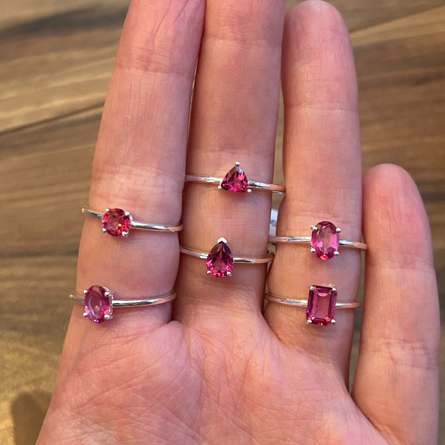 hand wearing five vibrant pink topaz rings with gemstones in various shapes on wooden background Ring Pure Pink Topaz