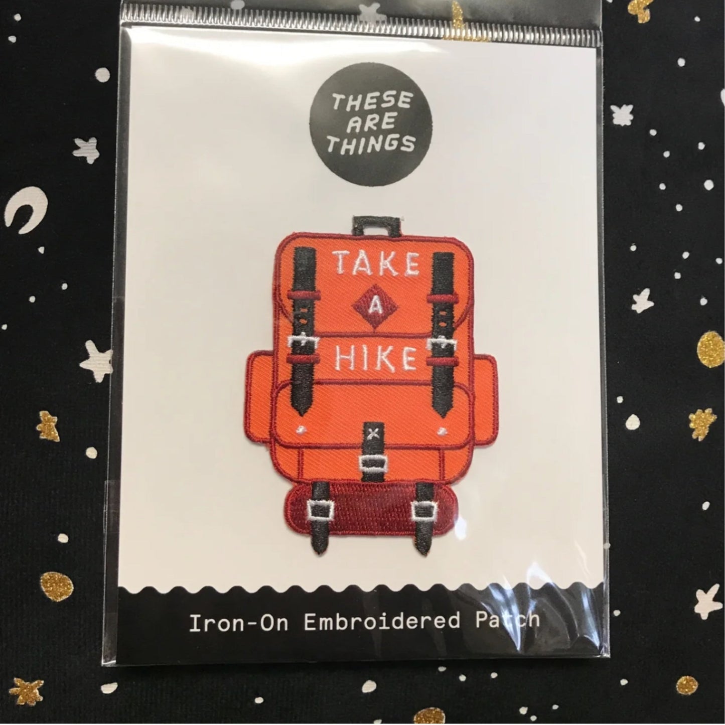 Take A Hike iron-on embroidered patch featuring an orange backpack design with hiking straps and text "TAKE A HIKE"