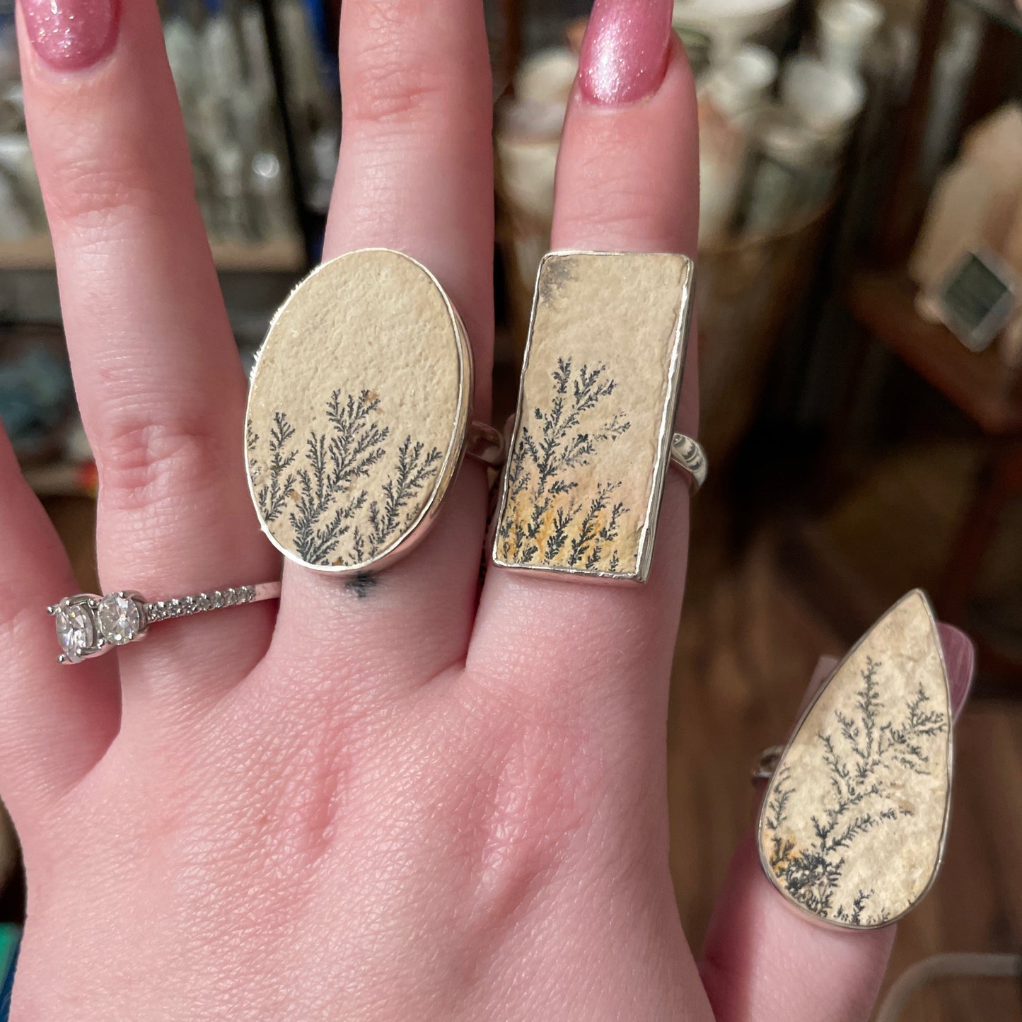 Hand wearing three adjustable Rings Psilomeiane Dendrite with unique dendrite stone patterns and one silver gemstone ring