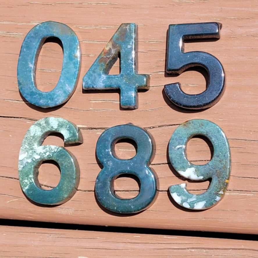 Moss agate number carving set featuring numbers 0, 4, 5, 6, 8, and 9 on wooden surface