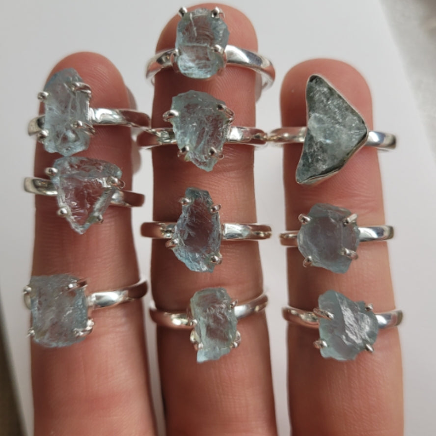 Collection of silver rings featuring raw aquamarine gemstones on fingers, showcasing natural and unique stone shapes and textures