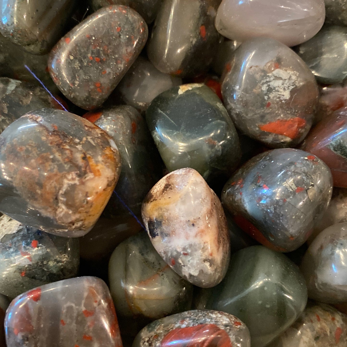 Close-up of polished Seftonite tumble stones with mixed gray, green, red, and brown hues for grounding and healing energy